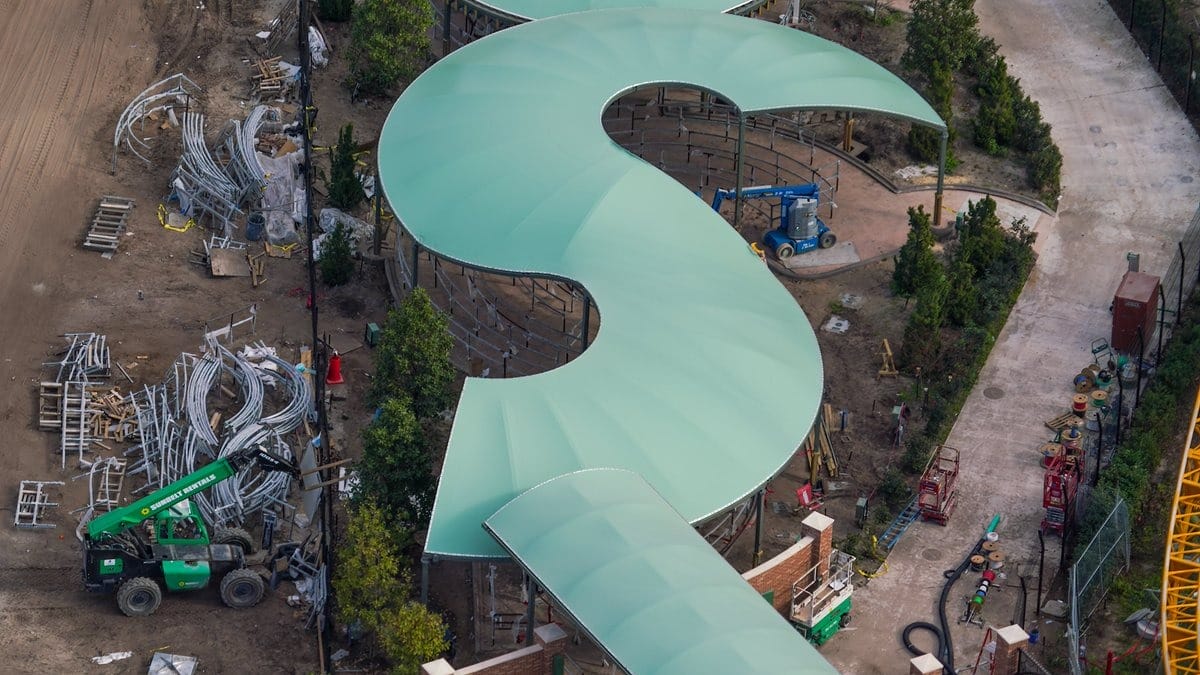 Aerial view of a curved, green-roofed structure under construction at the Epic Universe theme park, surrounded by building materials, machinery, and trees.