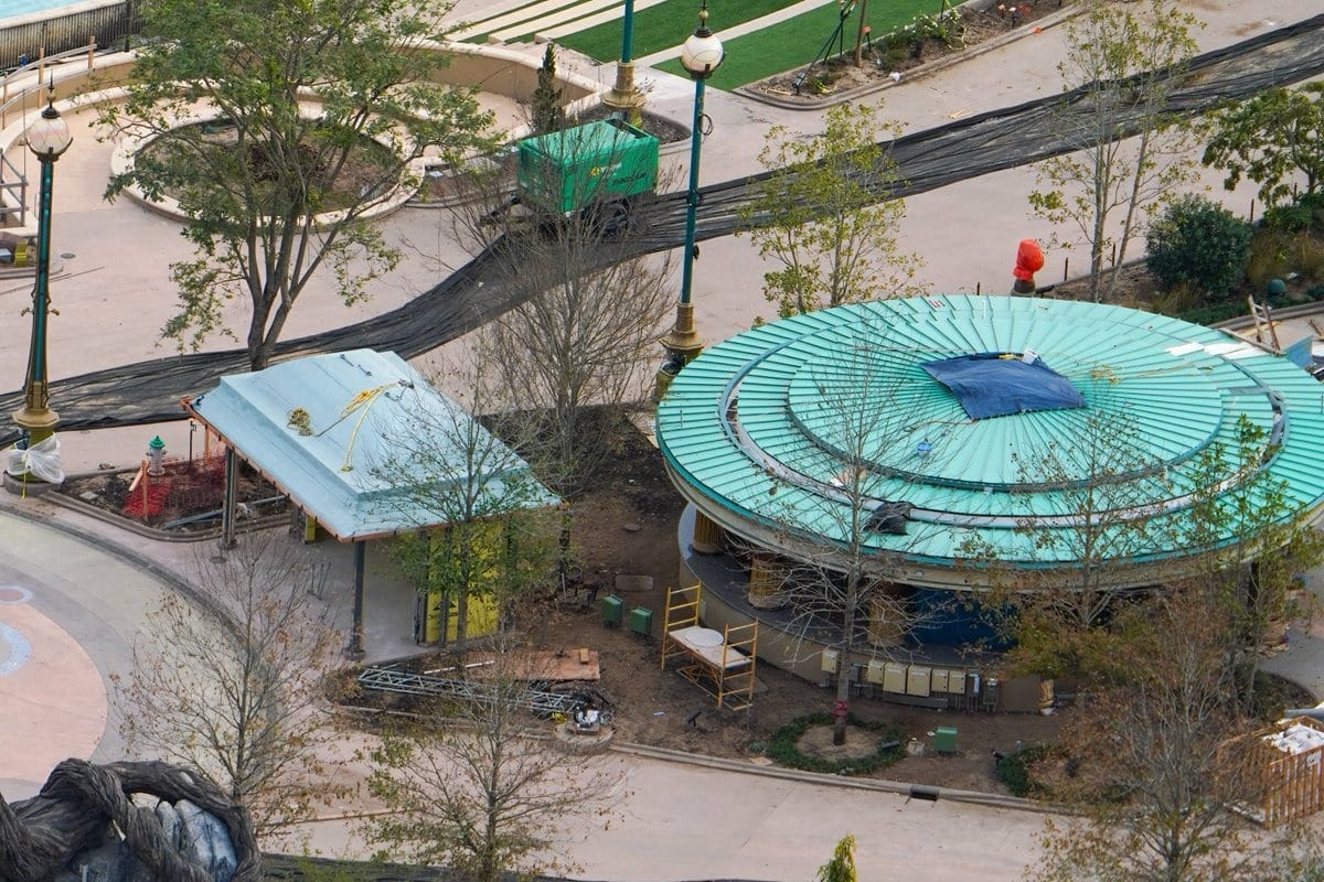 An aerial view captures the epic universe of a park under construction, featuring a circular building with a green roof and surrounding pathways. Construction materials and equipment are visible, while partially leafless trees hint at the natural transformation to come.