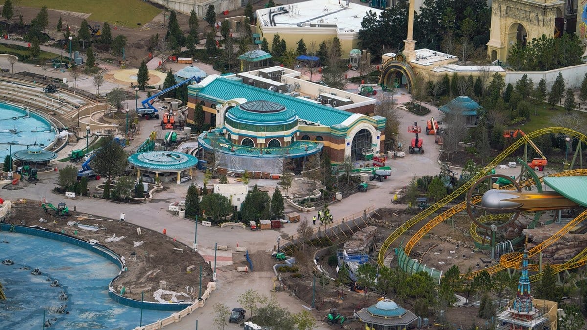 Aerial view of Epic Universe theme park under construction, revealing visible rides, pathways, and several construction vehicles and workers bustling about.