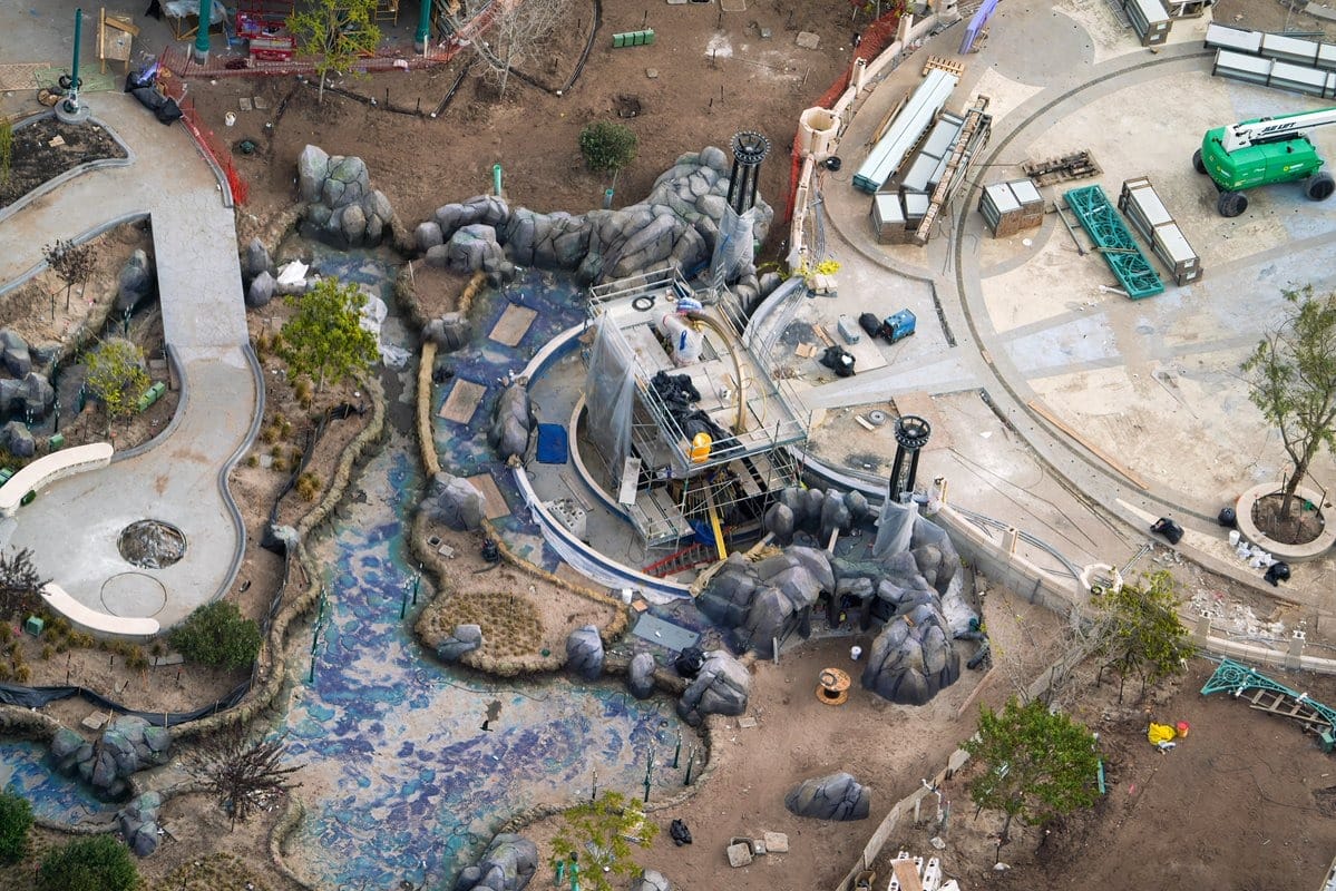 An epic universe unfolds from above, where pathways weave through rocky landscaping, converging at a central structure. Various equipment and materials are meticulously spread across the bustling construction site.