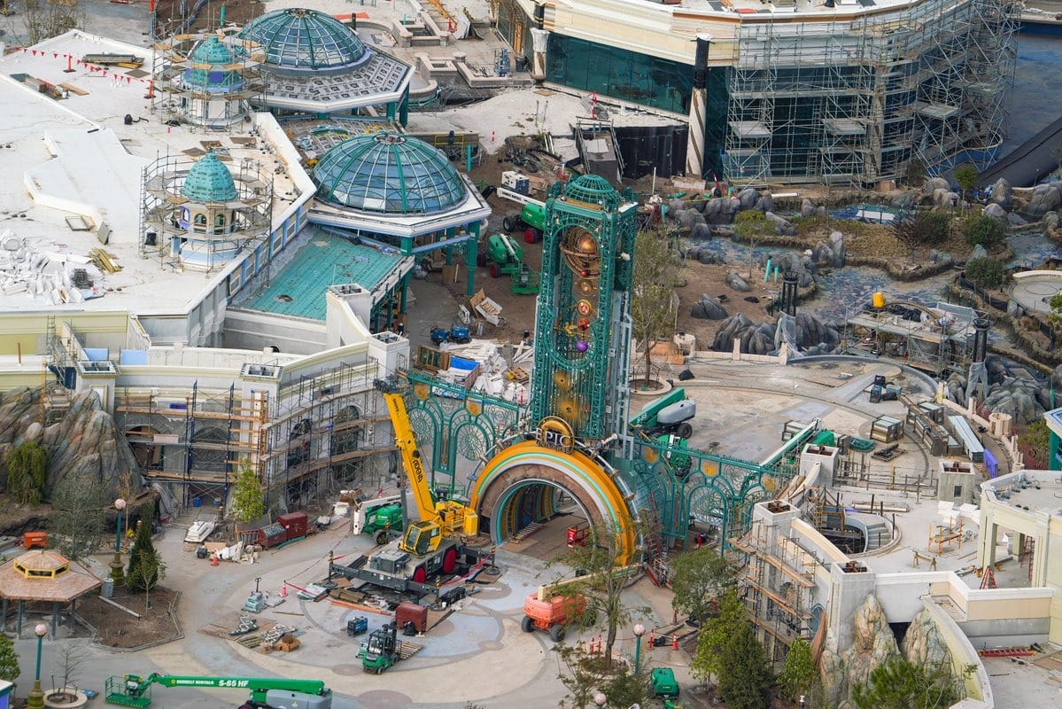 Aerial view of an epic universe-themed construction site, featuring scaffolding, machinery, and decorative structures in progress.