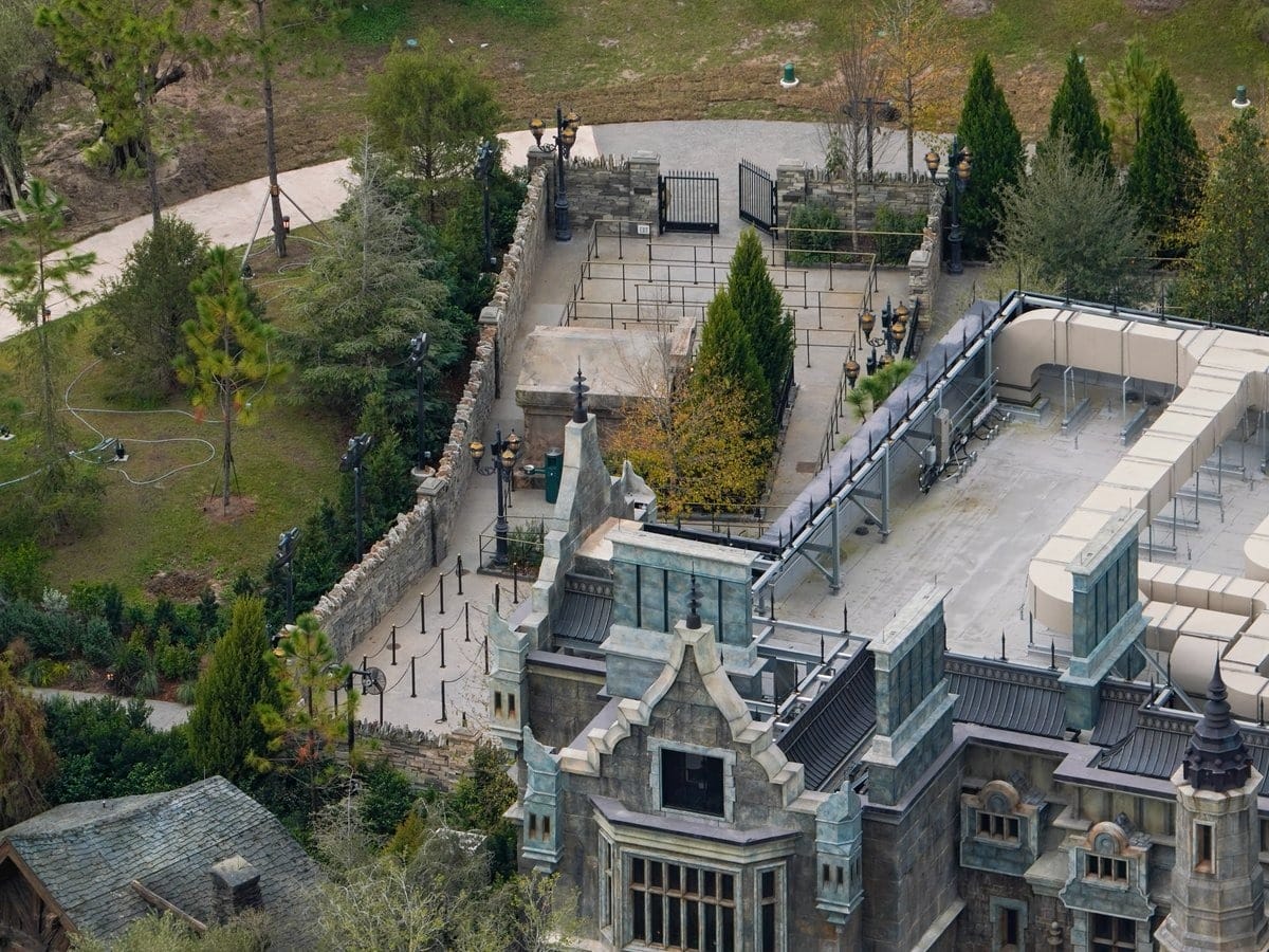 Aerial view of Epic Universe theme park building with intricate architecture, surrounded by trees and pathways at Universal Theme Park. Queue lines are visible near the entrance.