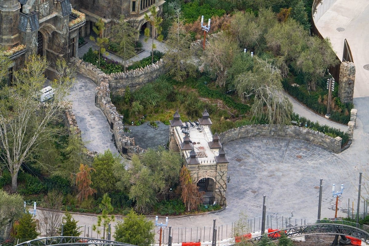 Aerial view of Epic Universe reveals castle-like structures, winding pathways, and lush greenery. Roller coaster tracks twist through this enchanting theme park, showcasing its thrilling attractions in the foreground.