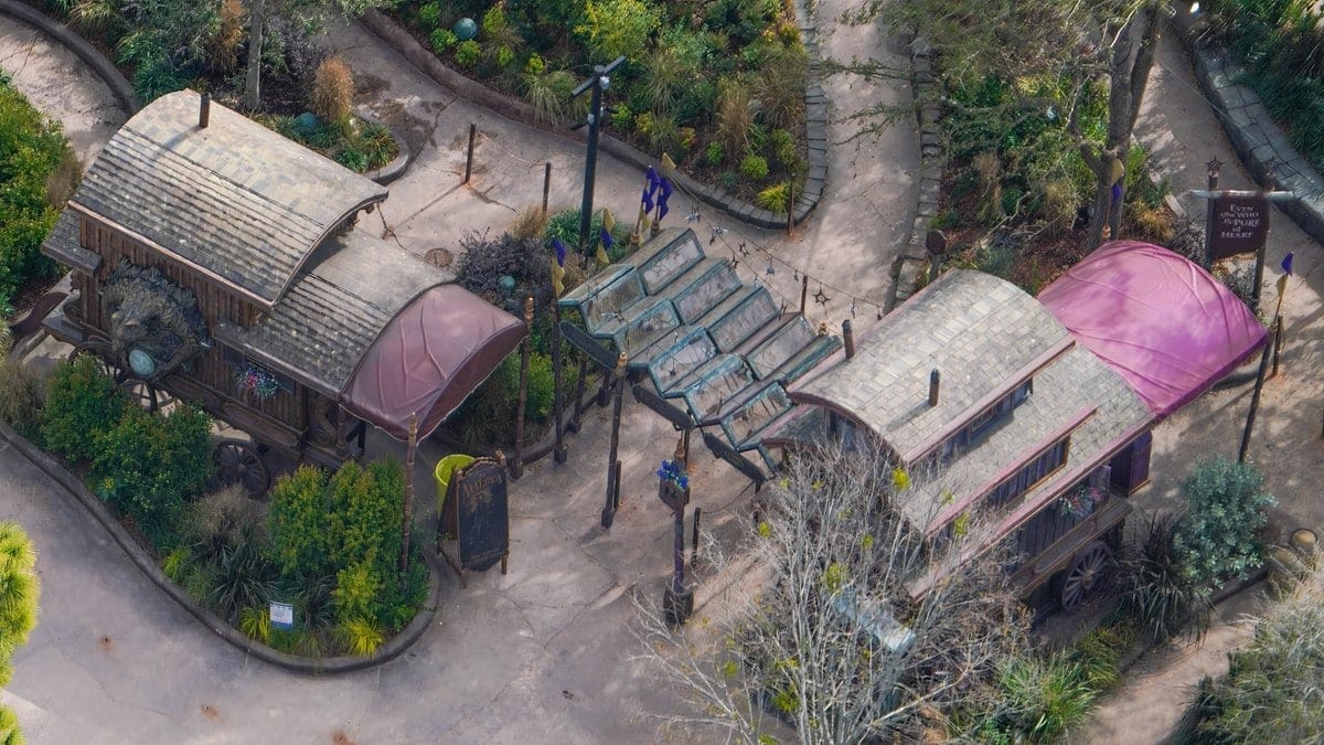 Aerial view of two whimsical wooden structures connected by a canopy, nestled in the lush greenery and pathways of an epic theme park setting that could easily find its home in Orlando's universe.