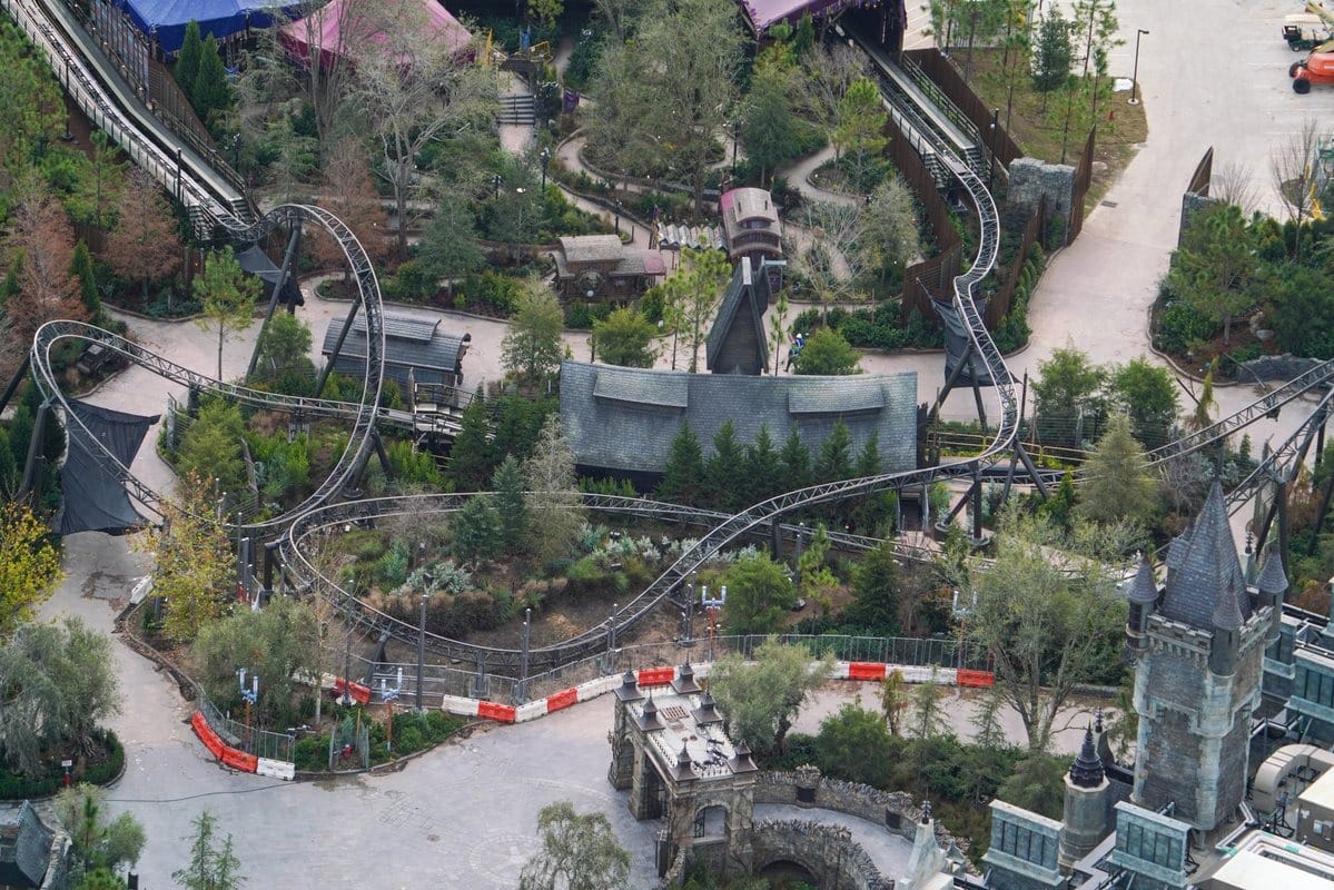 Aerial view of a roller coaster winding through a forested area at Universal Studios' Epic Universe, with nearby structures and pathways.