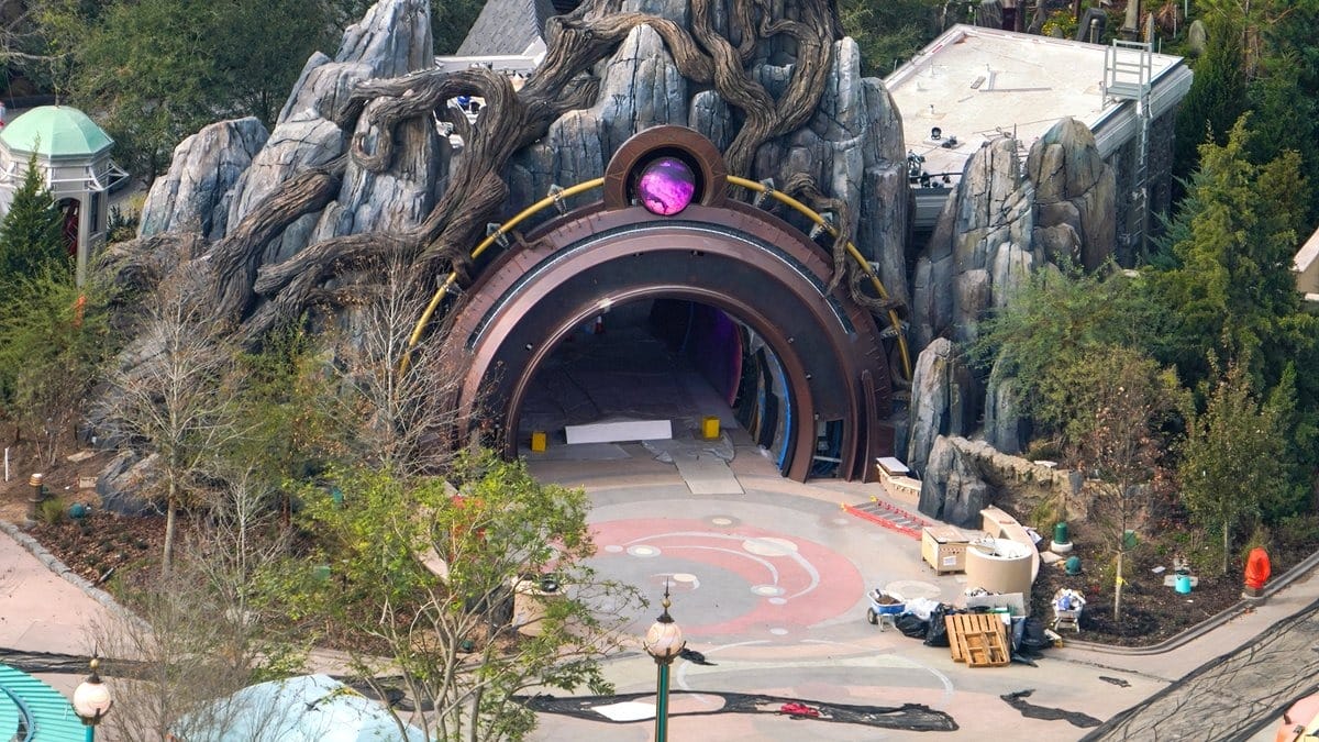 Aerial view of Epic Universe's stunning theme park attraction at Universal Orlando, featuring a rocky cave entrance with a circular doorway, nestled amidst lush trees.