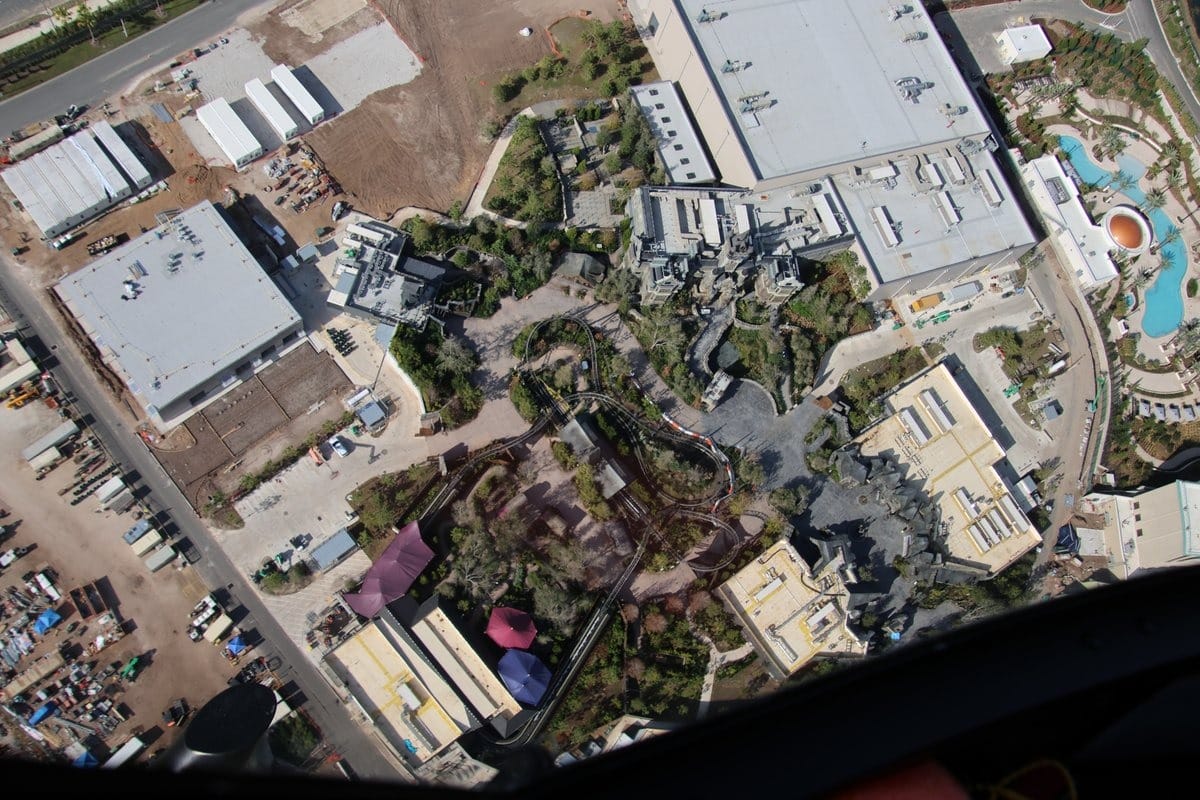 Aerial view of Epic Universe theme park under construction, revealing winding paths, buildings, and lush landscaping, all nestled within the bustling environs of parking and industrial areas.