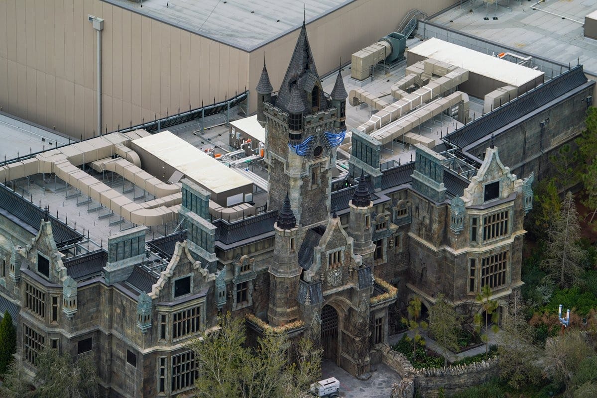 Aerial view of an epic castle-like building with pointed towers and intricate designs, seamlessly blending into the adjacent modern industrial rooftop structure, creating a universe of architectural contrasts.