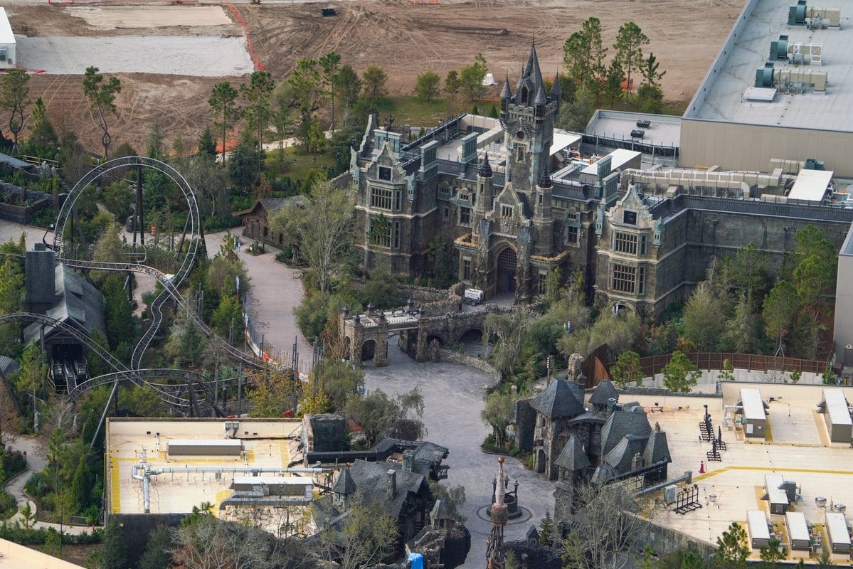 Aerial view of Epic Universe, an Orlando theme park, showcasing a gothic-style castle and roller coaster nestled among lush trees. Construction sites dot the background, hinting at exciting developments on the horizon.