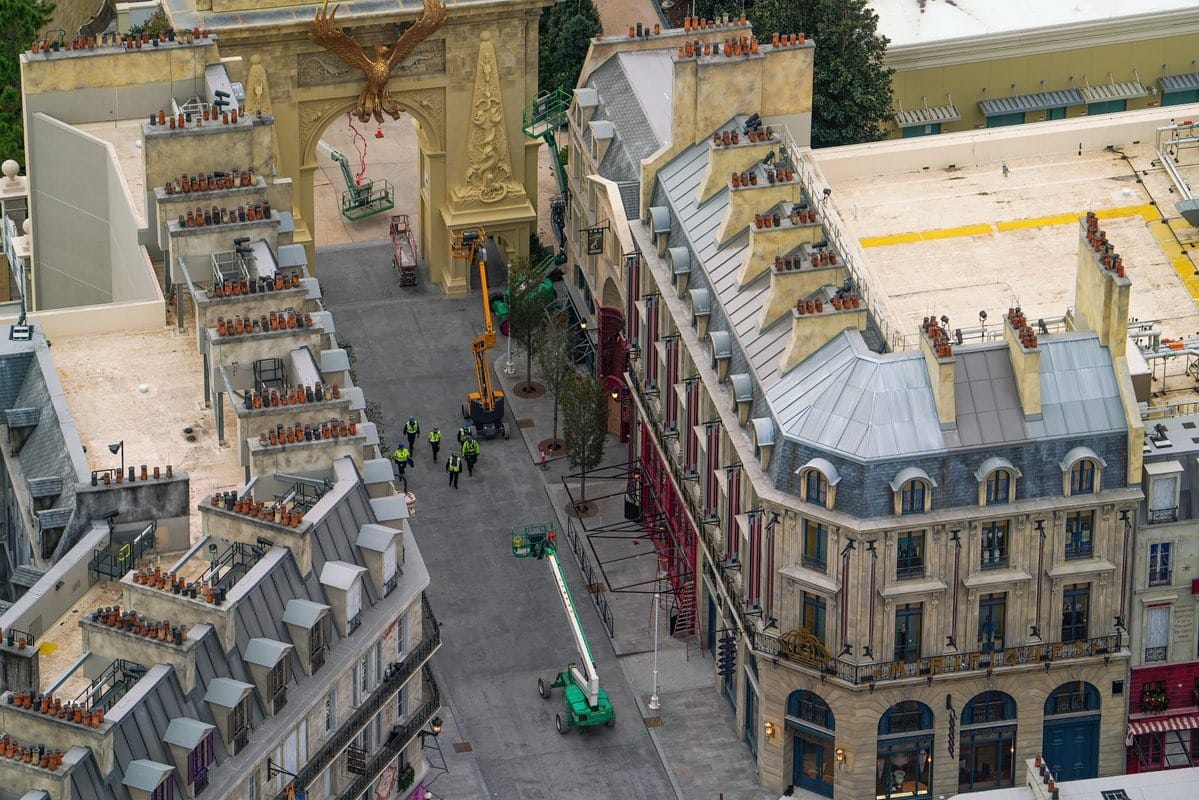 Aerial view of a street with construction machinery and workers near ornate European-style buildings with mansard roofs and decorative elements.
