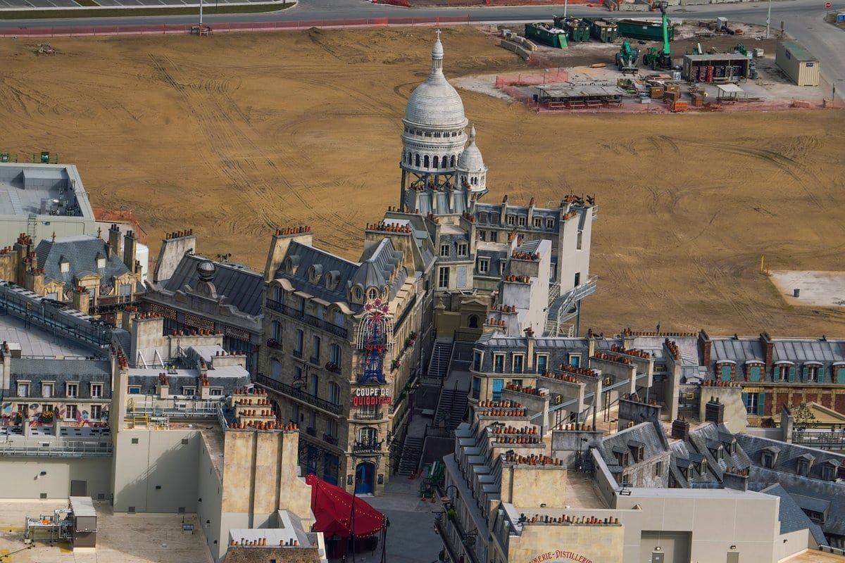 Aerial view of a film set in Epic Universe, designed to resemble a European cityscape with a prominent dome and surrounding streets, reminiscent of a Universal theme park under development with construction equipment nearby.