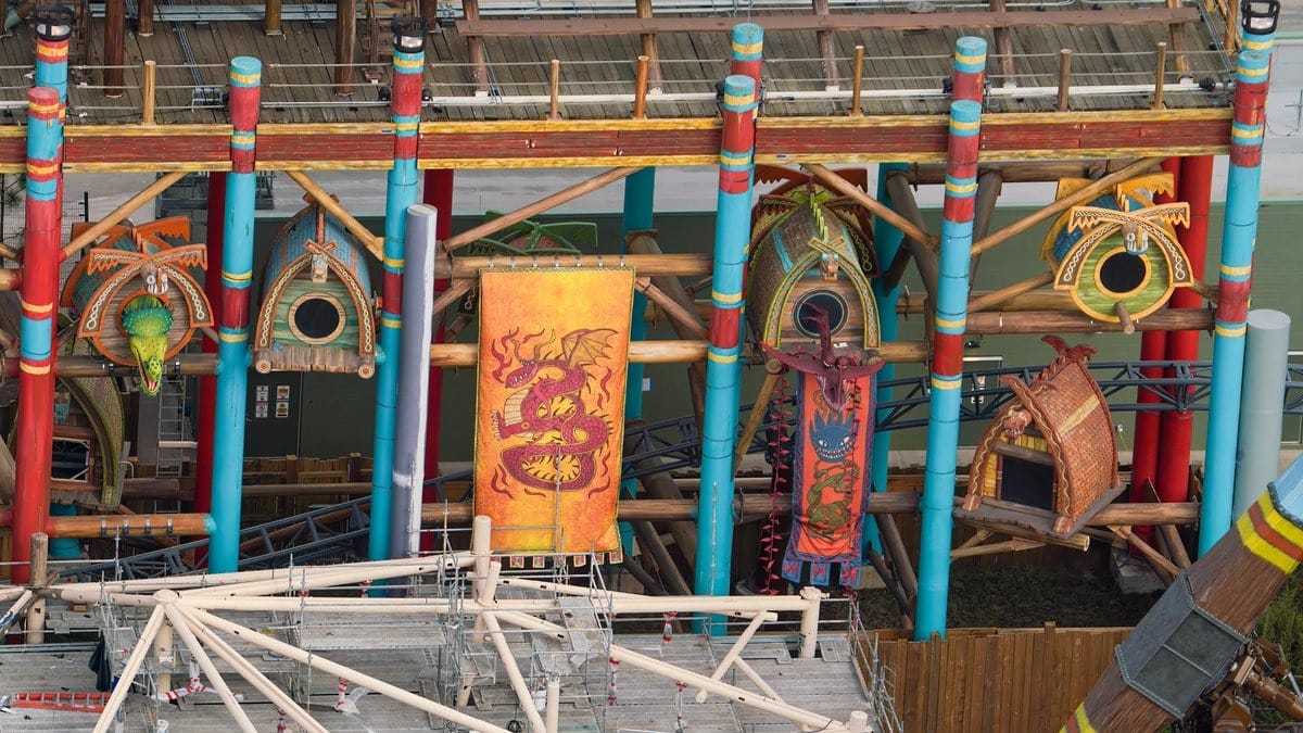 Colorful wooden structures with dragon-themed banners and climbing frames, featuring vibrant red, yellow, and green designs against a backdrop of a building and scaffolding.