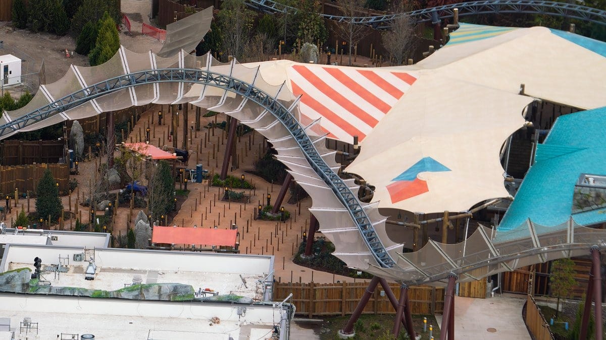 Aerial view of an outdoor amusement attraction featuring winding pathways, colorful tented structures, and surrounding greenery.