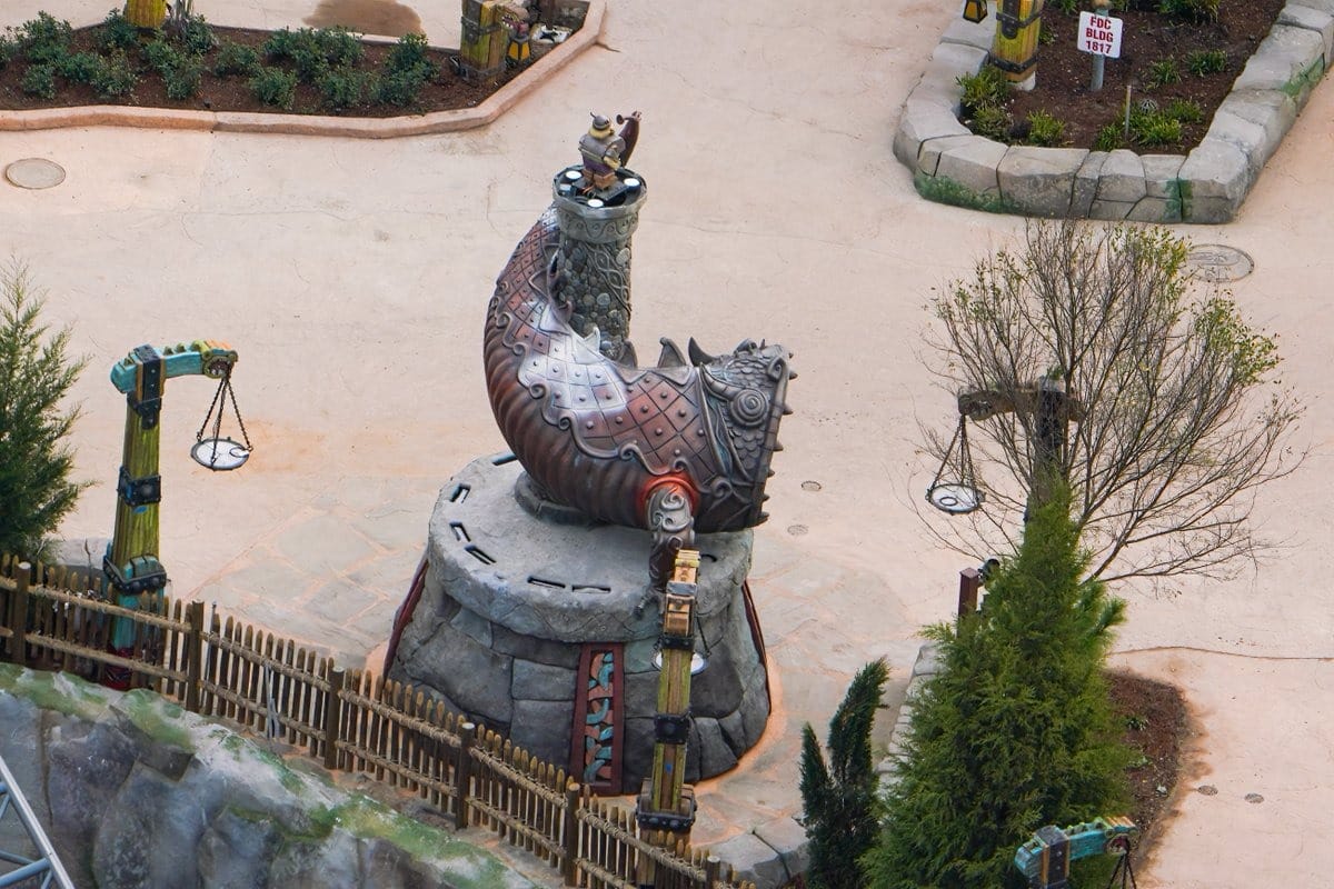 Aerial view of a whimsical, horn-shaped water fountain sculpture in an outdoor park, surrounded by trees and stone pathways.