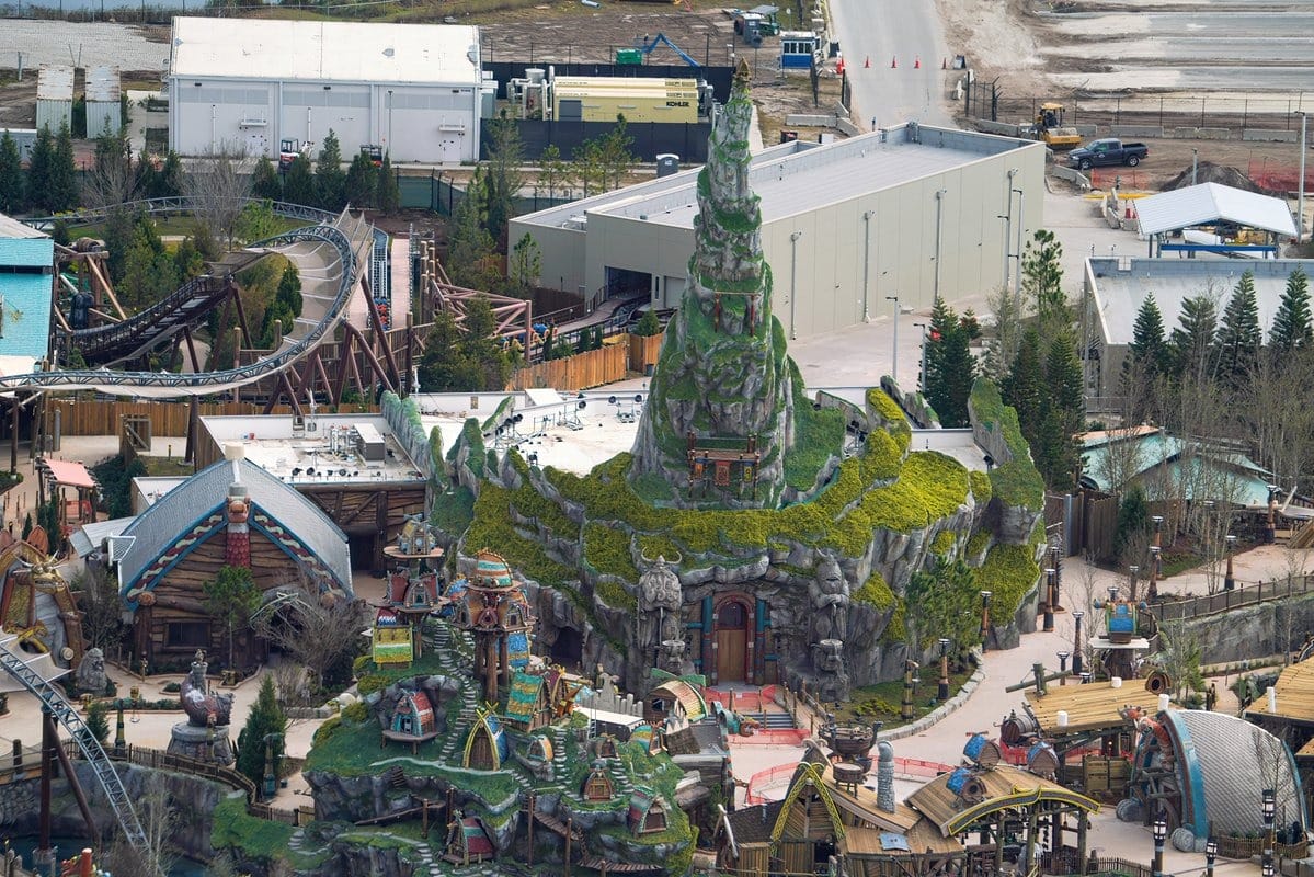 Aerial view of a theme park with a large, intricately designed mountain structure, various buildings, and winding roller coaster tracks.