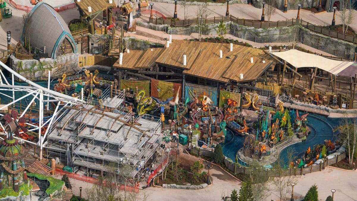 Aerial view of a theme park attraction with vibrant decor and a winding water feature. Construction scaffolding is visible on a section of the attraction.