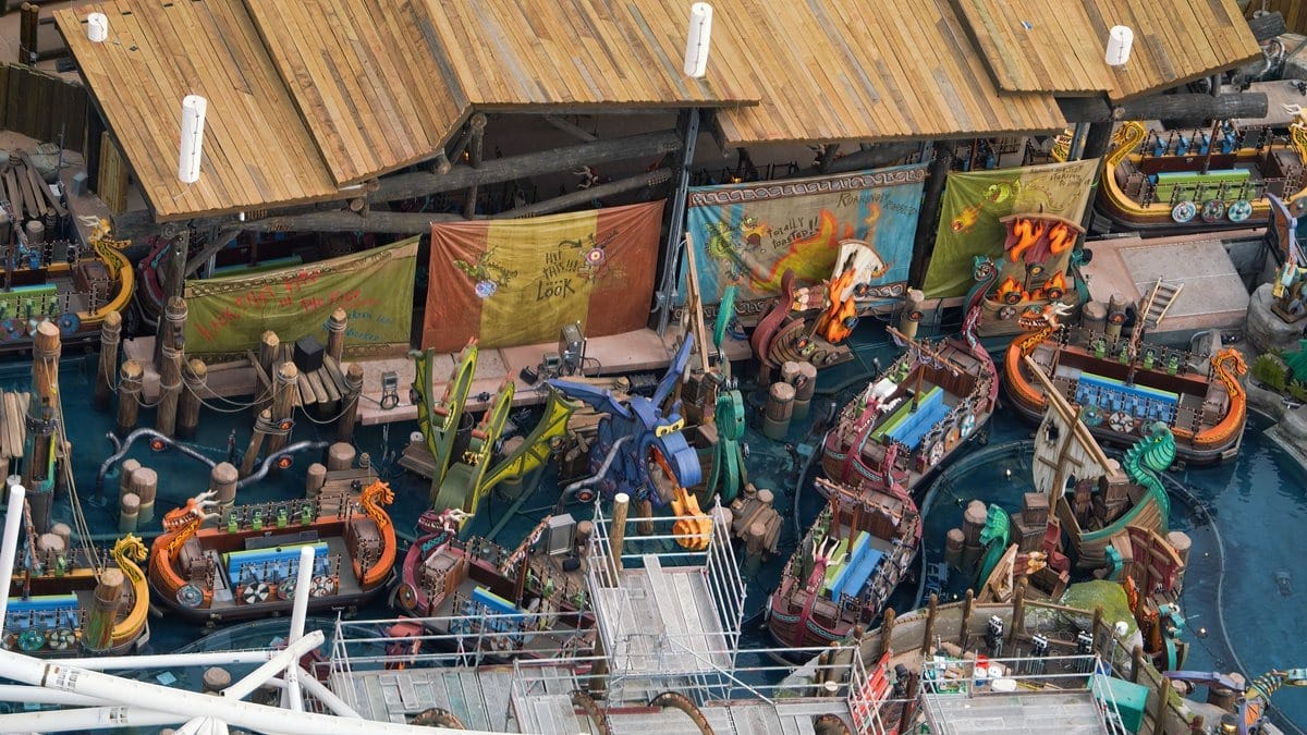 Aerial view of a theme park ride featuring viking-themed boats on a water track, with colorful banners and a wooden canopy overhead.