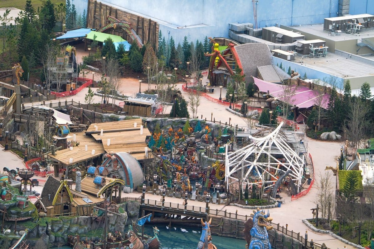Aerial view of a theme park under construction with various structures, pathways, and partially assembled rides surrounded by trees and pathways.