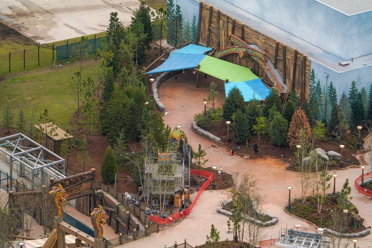 Aerial view of a theme park area under construction, featuring paths, scaffolding, and themed decorations surrounded by trees.