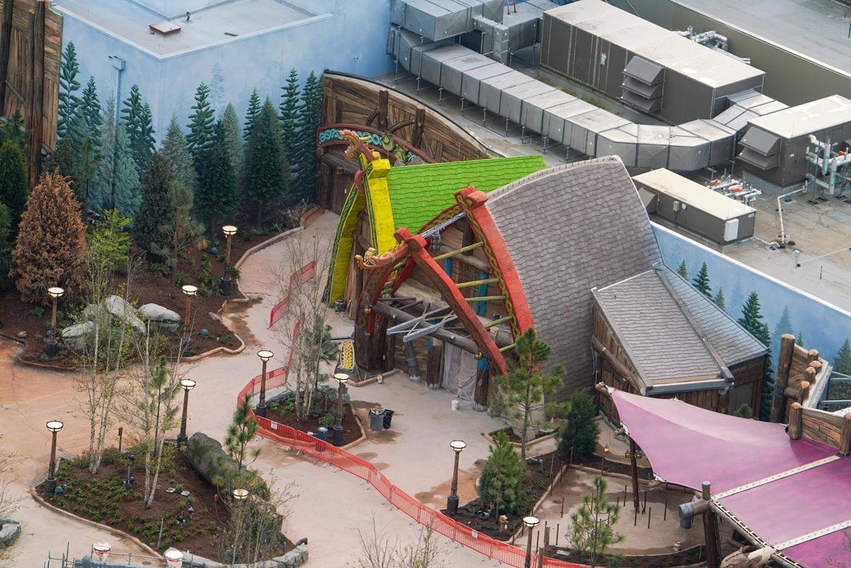 Aerial view of a colorful amusement park building with a bright roof, surrounded by trees and paths.