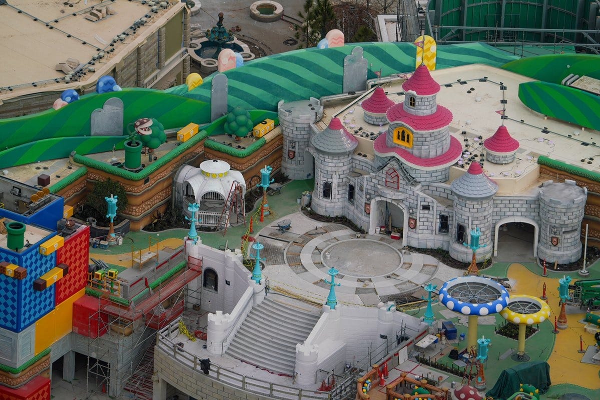 Aerial view of a colorful theme park construction site featuring a castle with red domes, surrounded by various play structures and vibrant pathways.