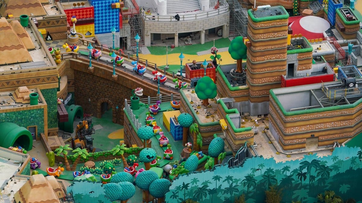 Aerial view of a colorful theme park featuring mushroom, brick, and tree elements. Pathways are lined with patterned walkways and decorative sculptures, surrounded by various vibrant structures.