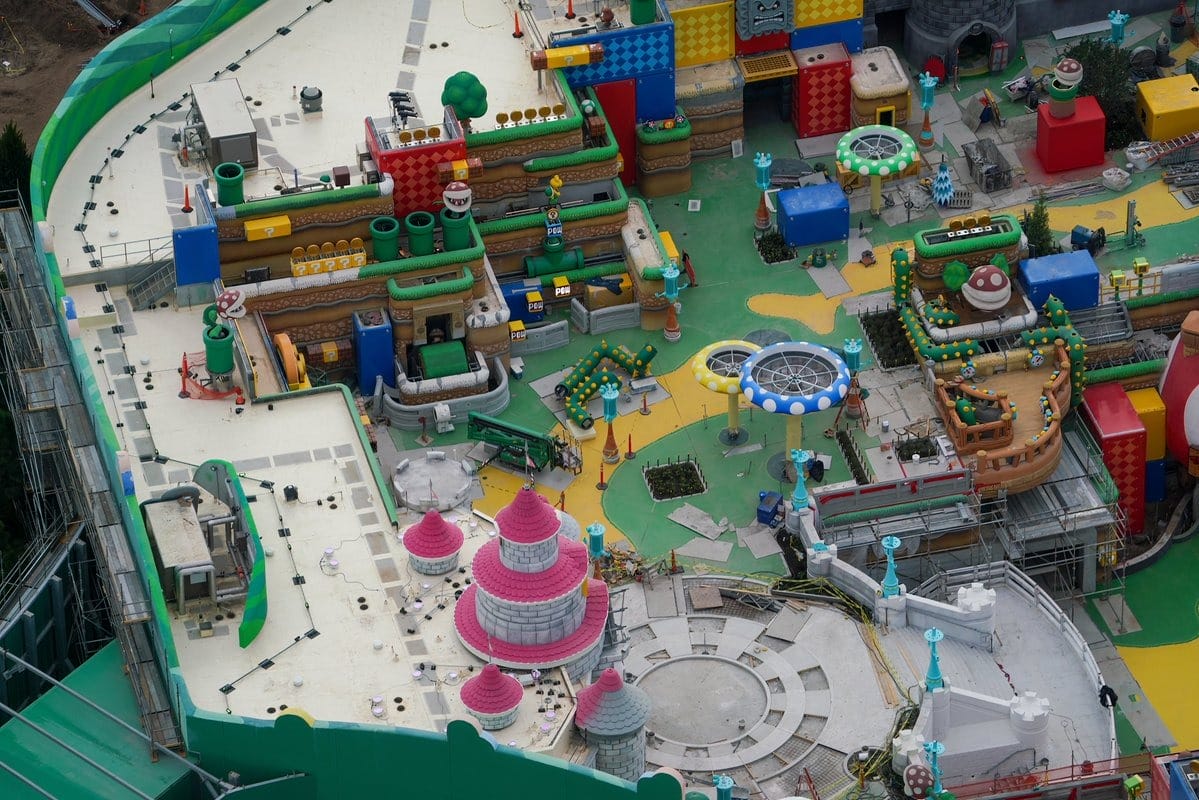 Aerial view of a colorful theme park construction site with various structures, tubes, and pathways in progress, surrounded by scaffolding.