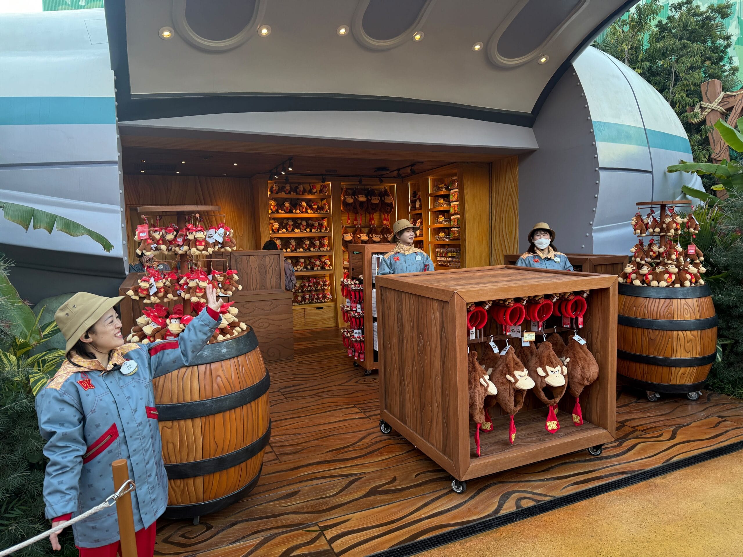 In Funky's Fly n Buy, a lively theme park gift shop, three staff members in uniform stand proudly beside vibrant displays of plush toys and unique merchandise.