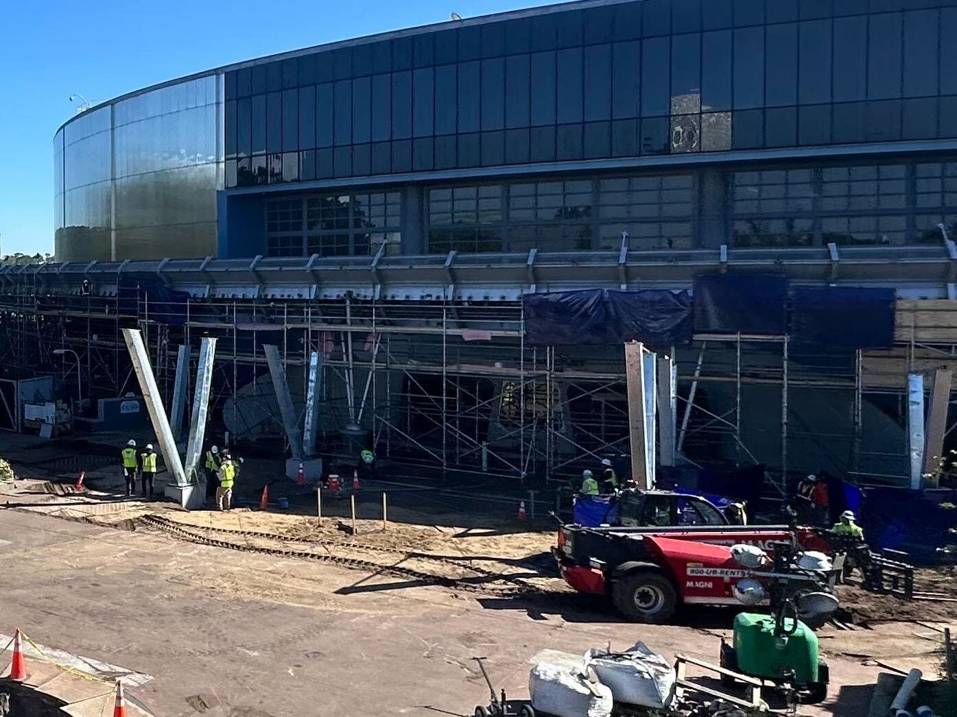 A Test Track hums with activity as workers and machinery bustle around a large glass-paneled building. The site is alive with scaffolding, steel beams, and construction prowess on full display.