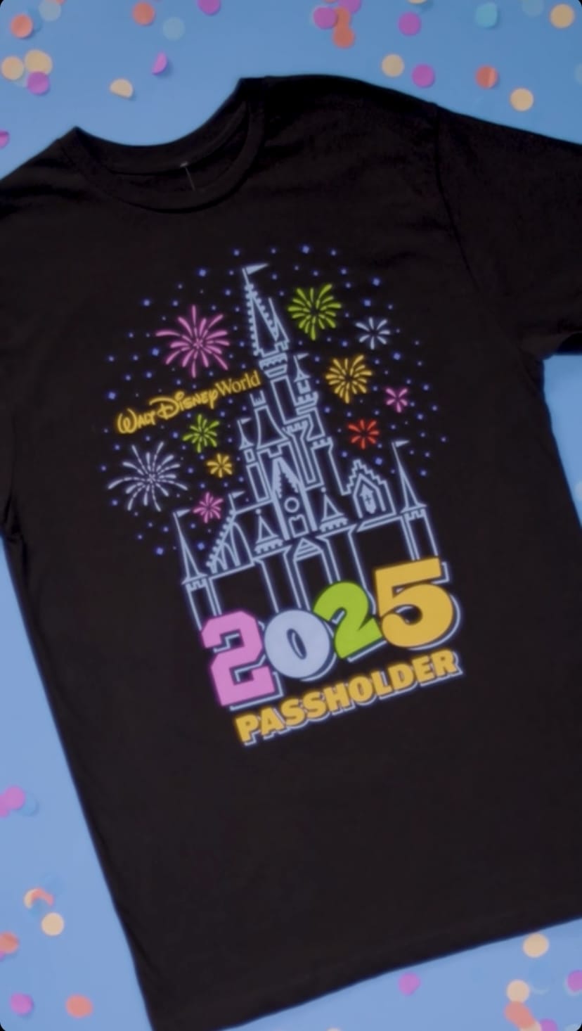 Black T-shirt with a colorful design of a castle, fireworks, and the words "Walt Disney World 2025 Passholder" on a confetti background.
