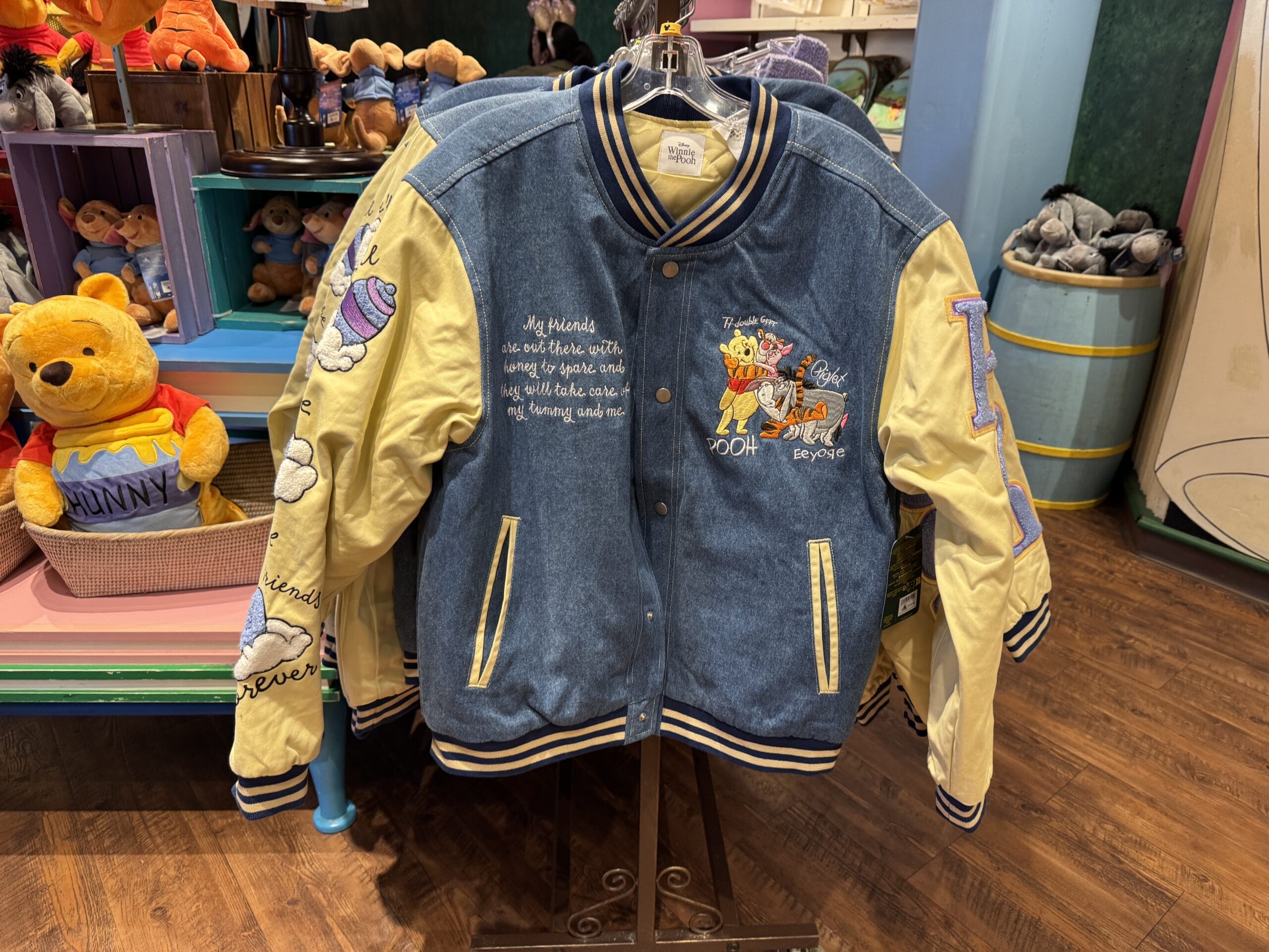 A photo report captures a vibrant blue and yellow varsity jacket with cartoon embroidery displayed on a wooden floor, evoking the whimsical charm of Magic Kingdom in 2024.