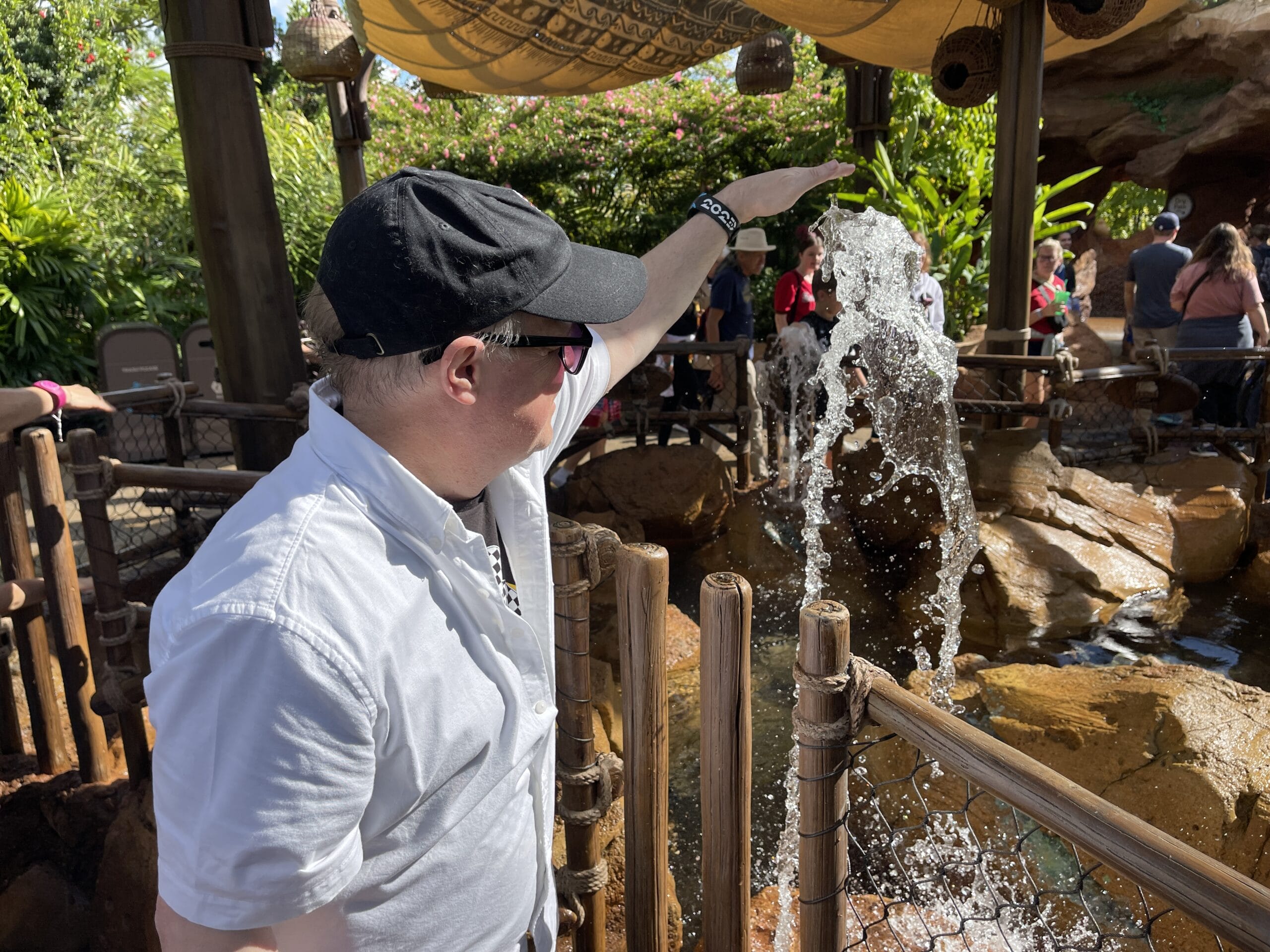 A man in sunglasses points at water shooting up in the Moana: Journey of Water tropical-themed outdoor area.