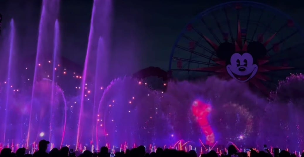 Experience the spectacular World of Color as vibrant water fountains and an enchanting light show illuminate the Ferris wheel, featuring a playful character face in celebration of Lunar New Year 2025.