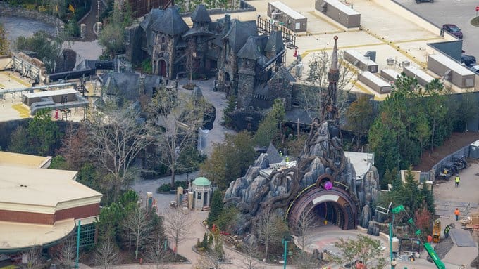 An aerial view reveals the Epic Universe theme park, showcasing its castle-like structures and rock formations amid bustling construction activity.