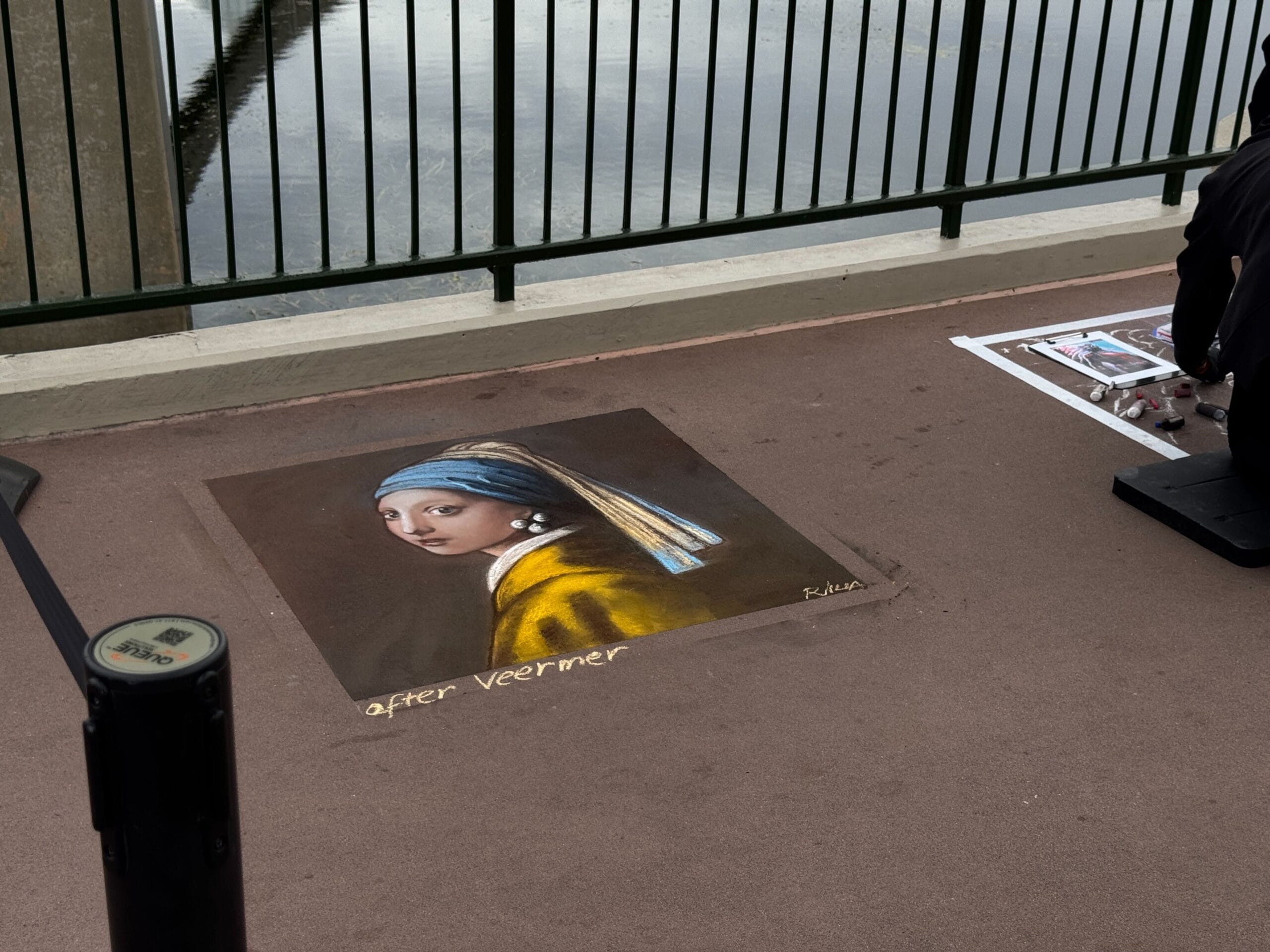 At the EPCOT Festival of the Arts, a talented artist brings "Girl with a Pearl Earring" to life in vivid chalk art on the pavement by a railing near water.