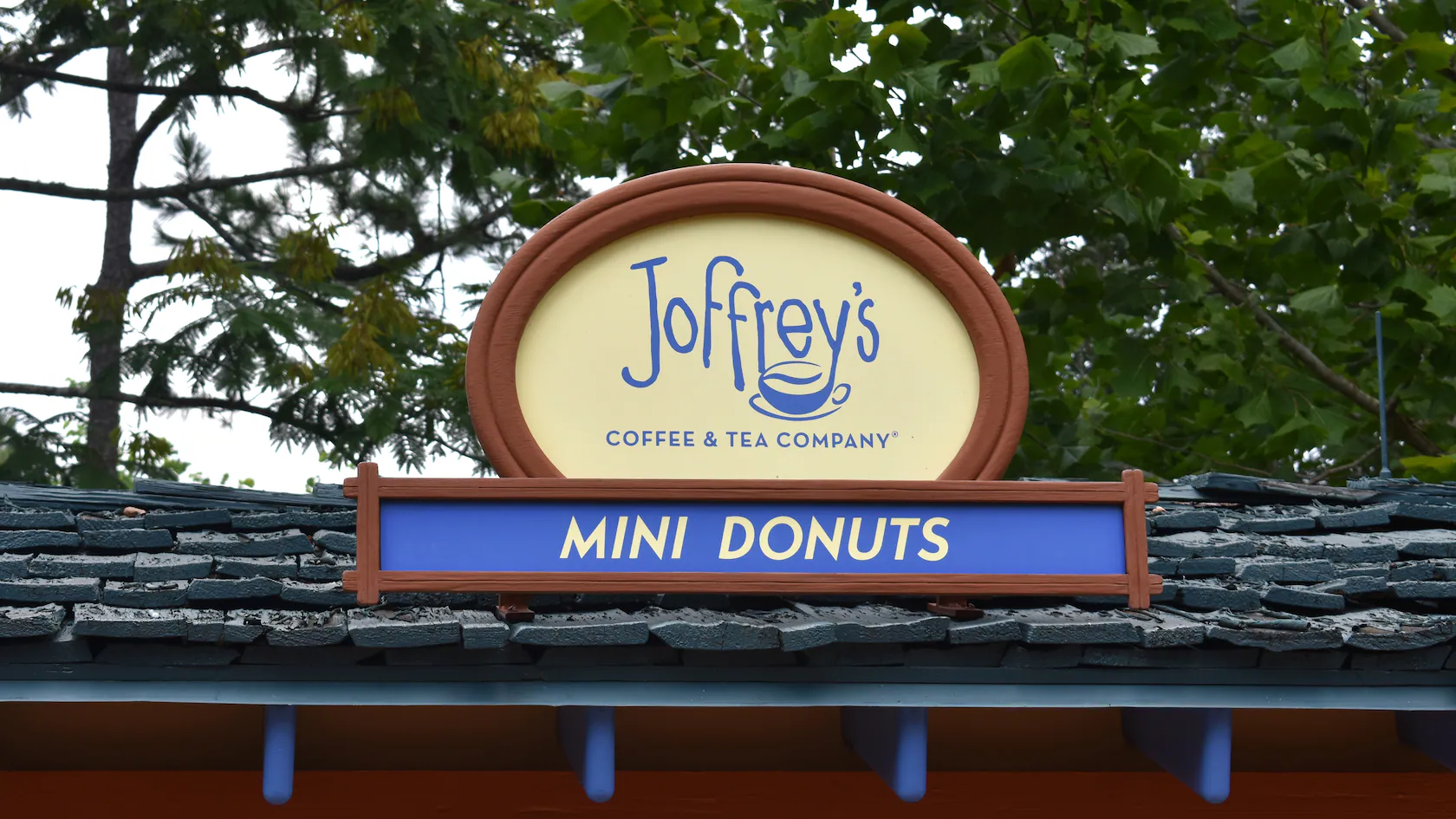 A Joffrey's Coffee sign with "MINI DONUTS" below, set against trees and shingles at Blizzard Beach.