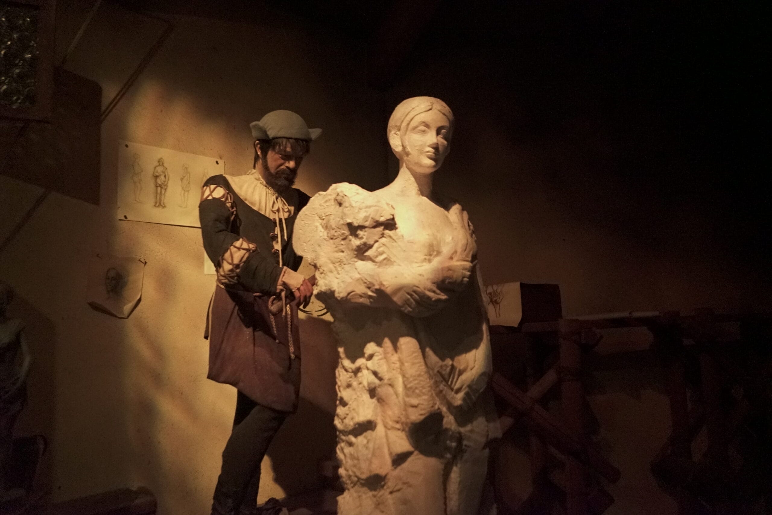 A man in period clothing sculpts a statue of a woman in a dimly lit workshop, evoking Spaceship Earth at Disney World.