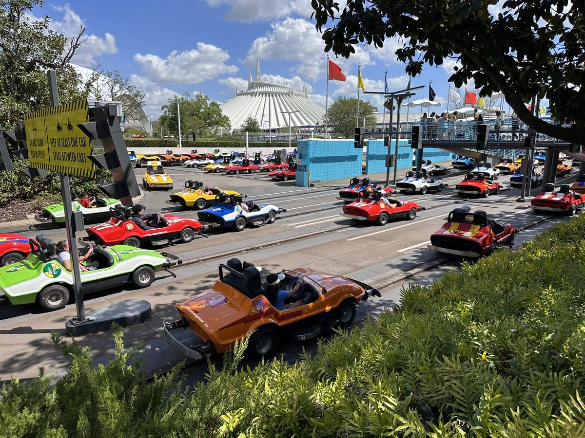 Colorful cars race on Tomorrowland Speedway at Magic Kingdom, with Space Mountain and flags in the background.