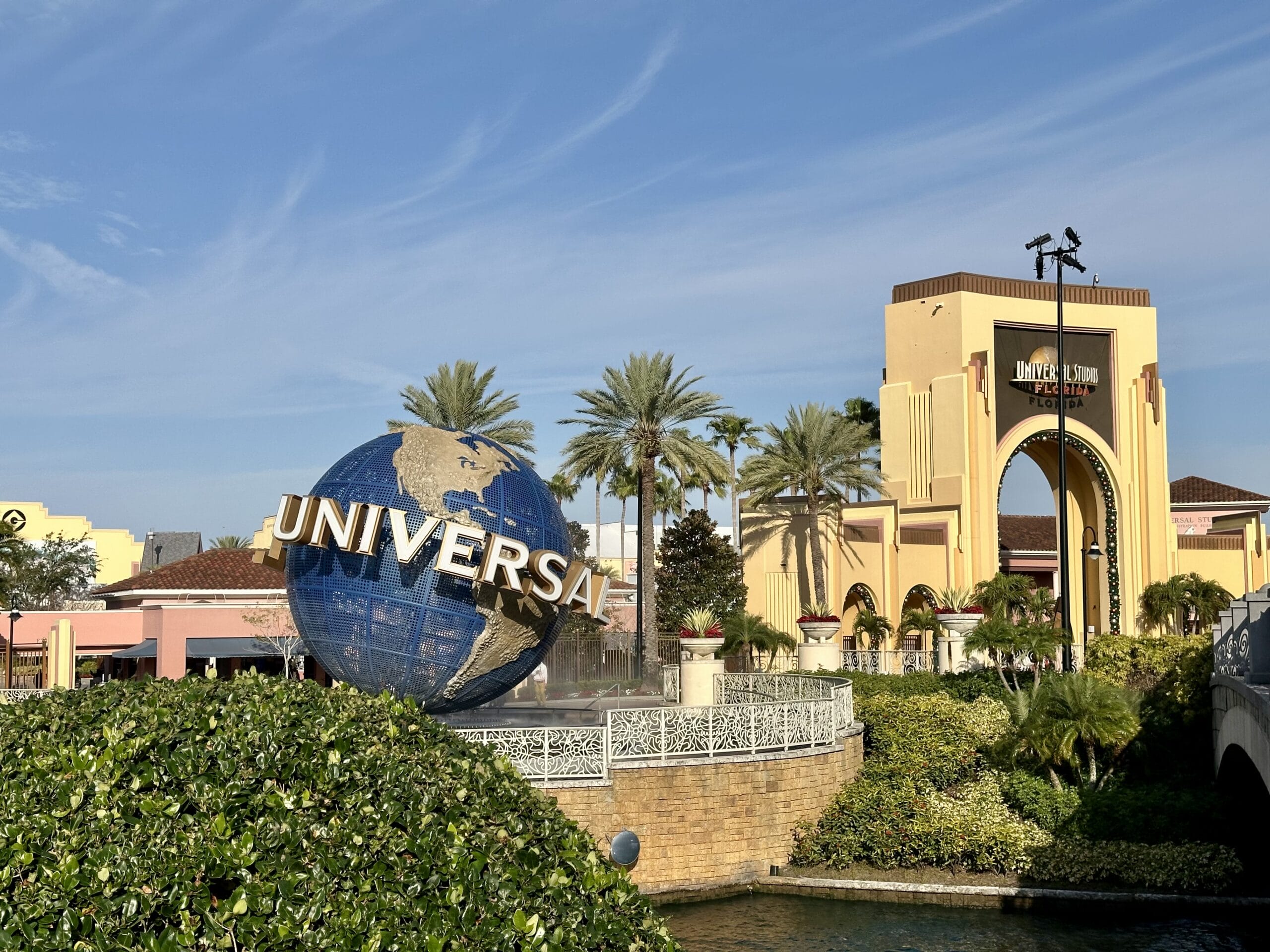 Universal Studios entrance with iconic globe sculpture, palm trees, and clear sky.