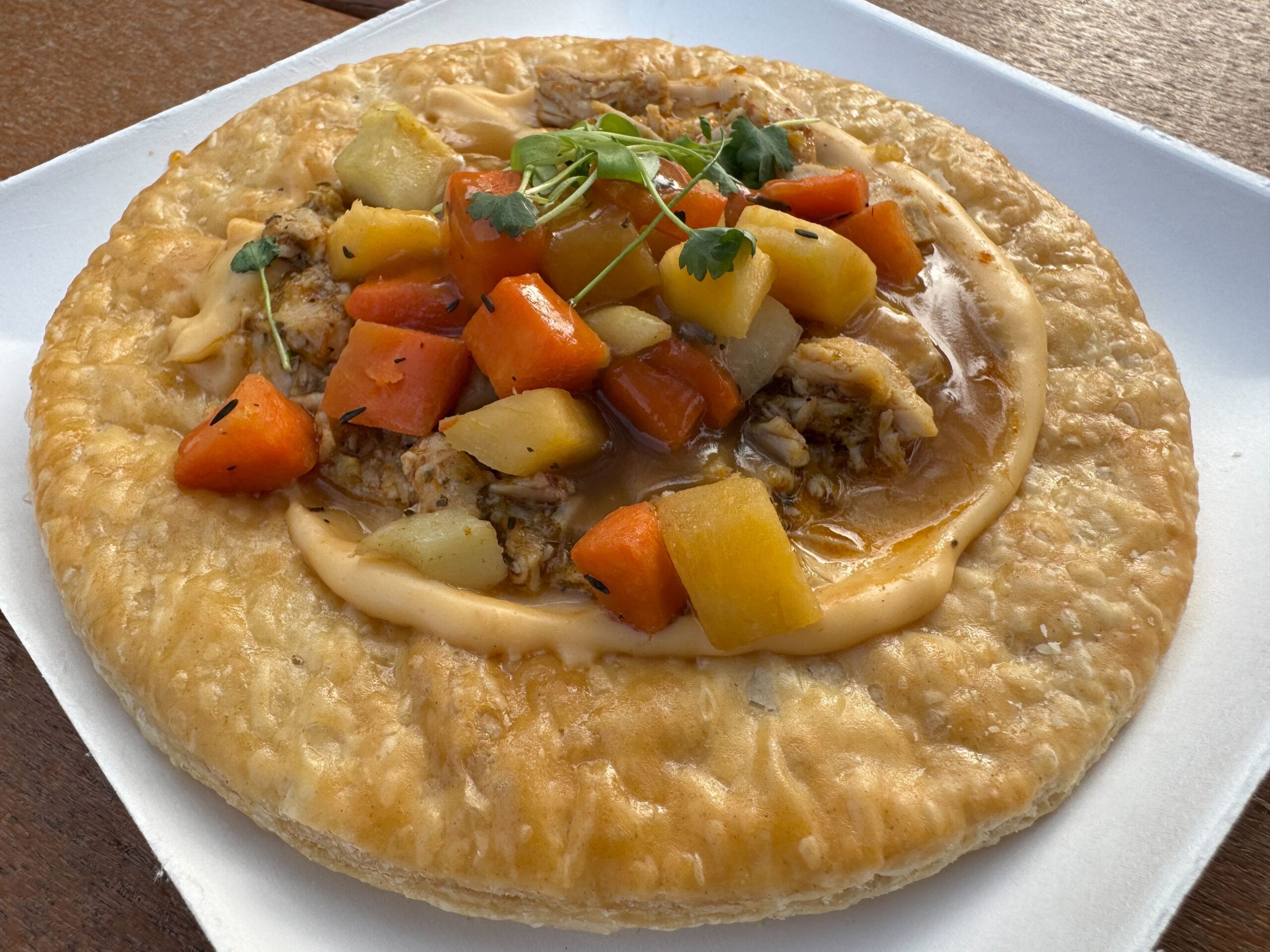 A savory pie topped with chunks of carrots, potatoes, and gravy, garnished with greens, evokes the creativity celebrated at the Festival of the Arts, served elegantly on a white plate.