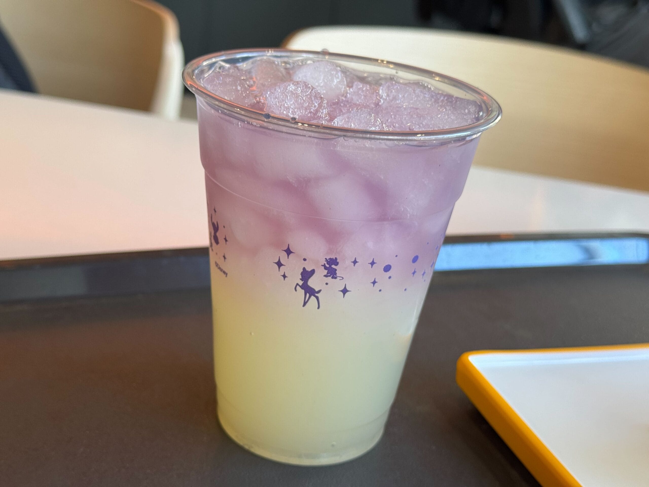 A pastel purple and yellow layered drink in a clear cup with ice, adorned with silhouettes and stars reminiscent of the Festival of the Arts.