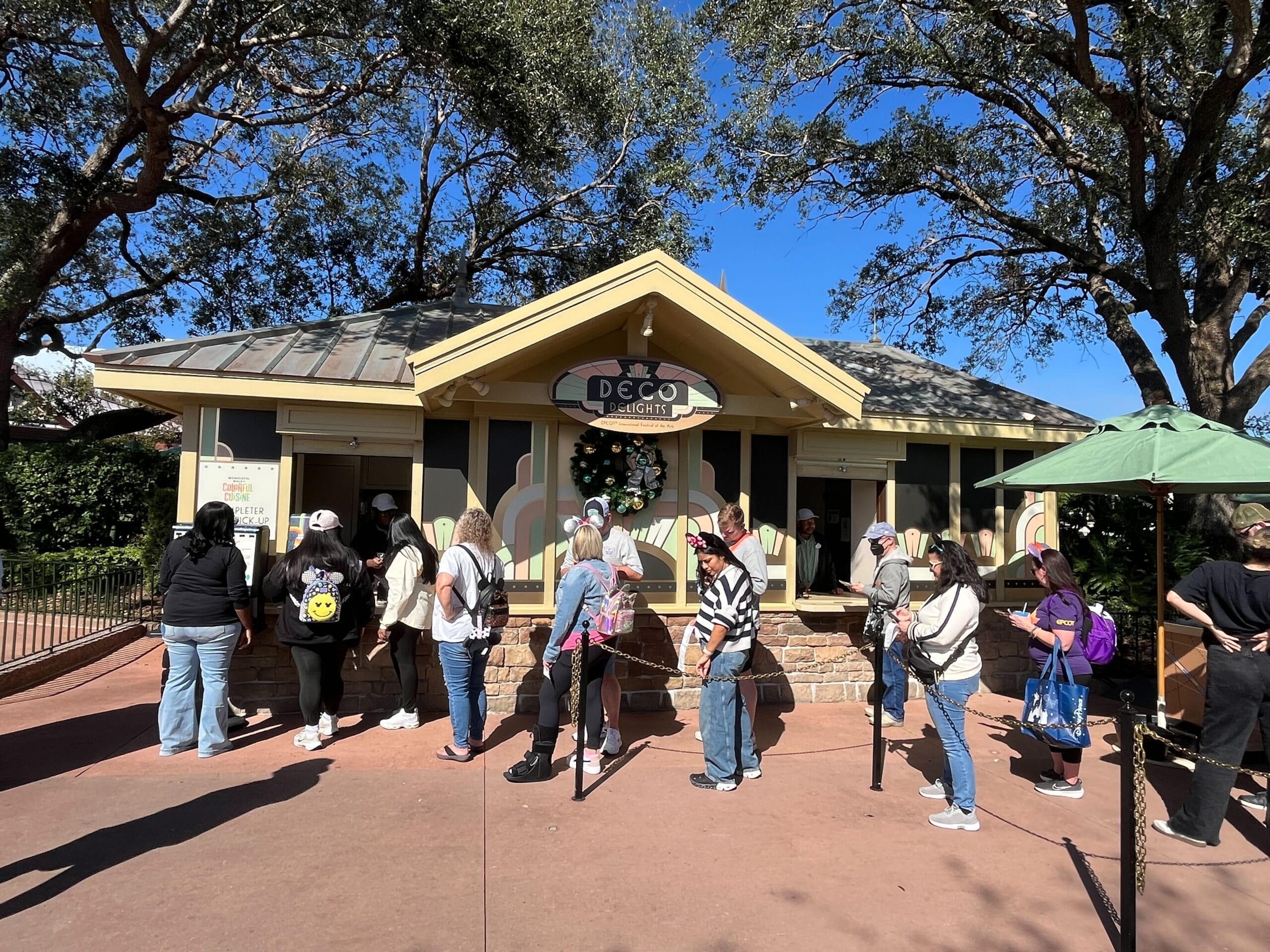 People lined up outside an ice cream stand named "Deco Delights" near the park, drawn by the vibrant Festival of the Arts atmosphere.
