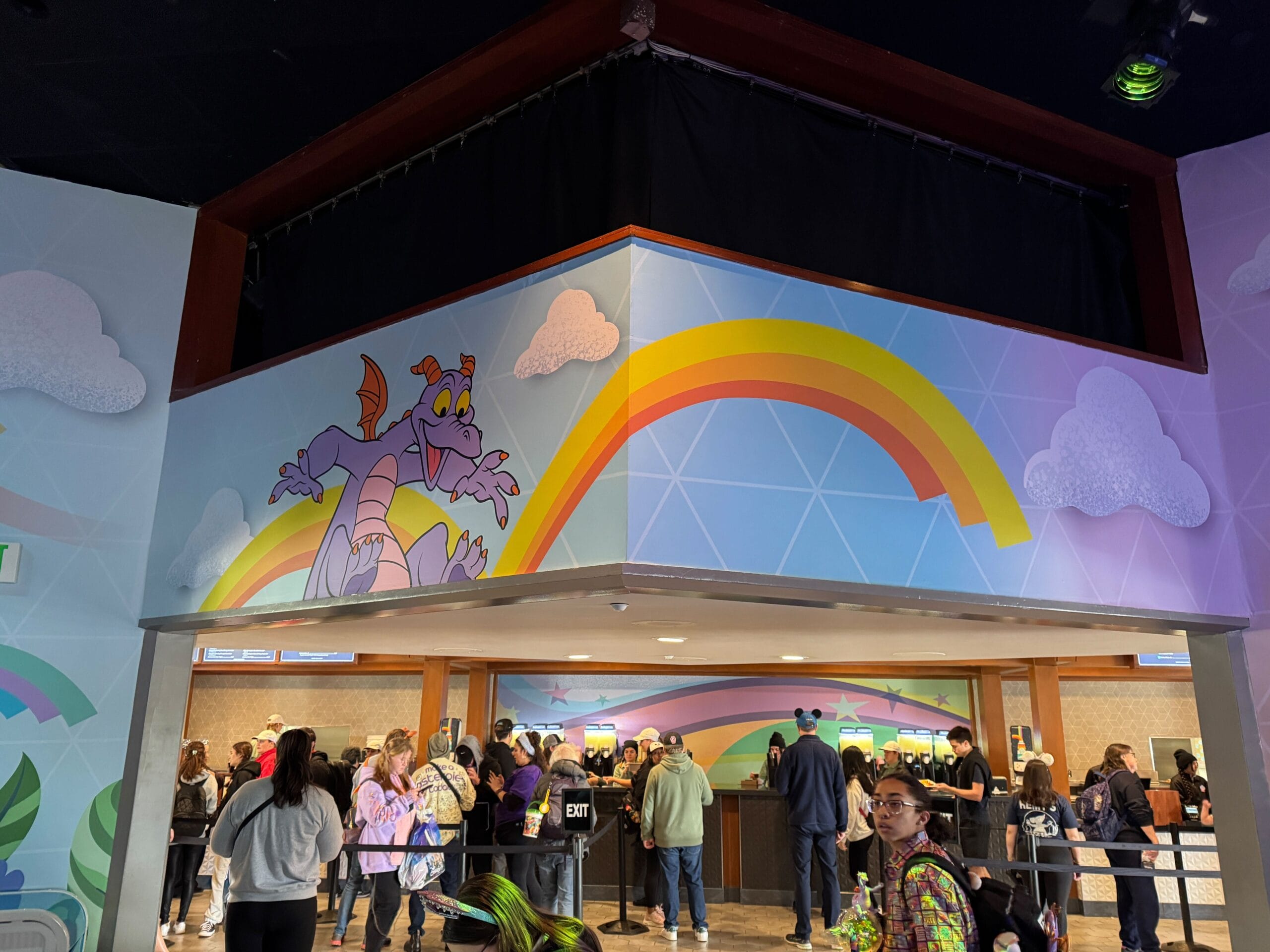 At the Festival of the Arts, people line up at a counter under a colorful mural featuring a purple dragon and rainbow on the wall.