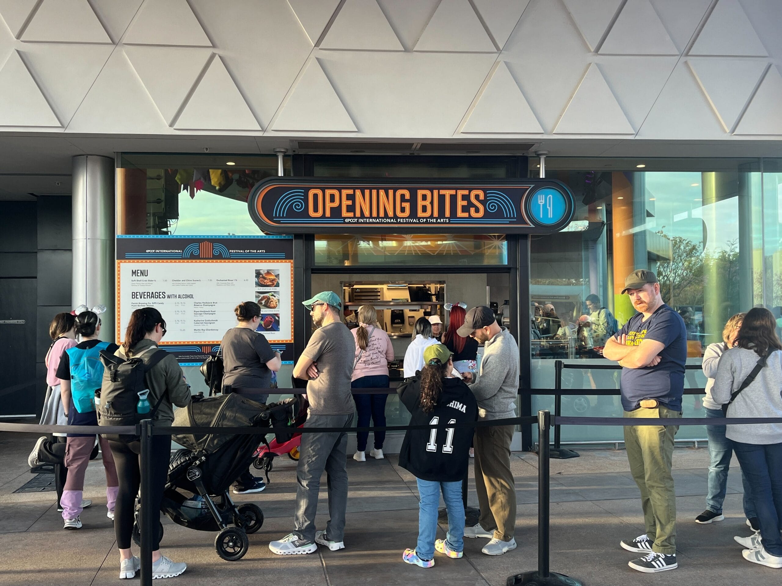 People eagerly lined up outside a food stand named "Opening Bites," where a vibrant menu was displayed, capturing the festive spirit of the Festival of the Arts.