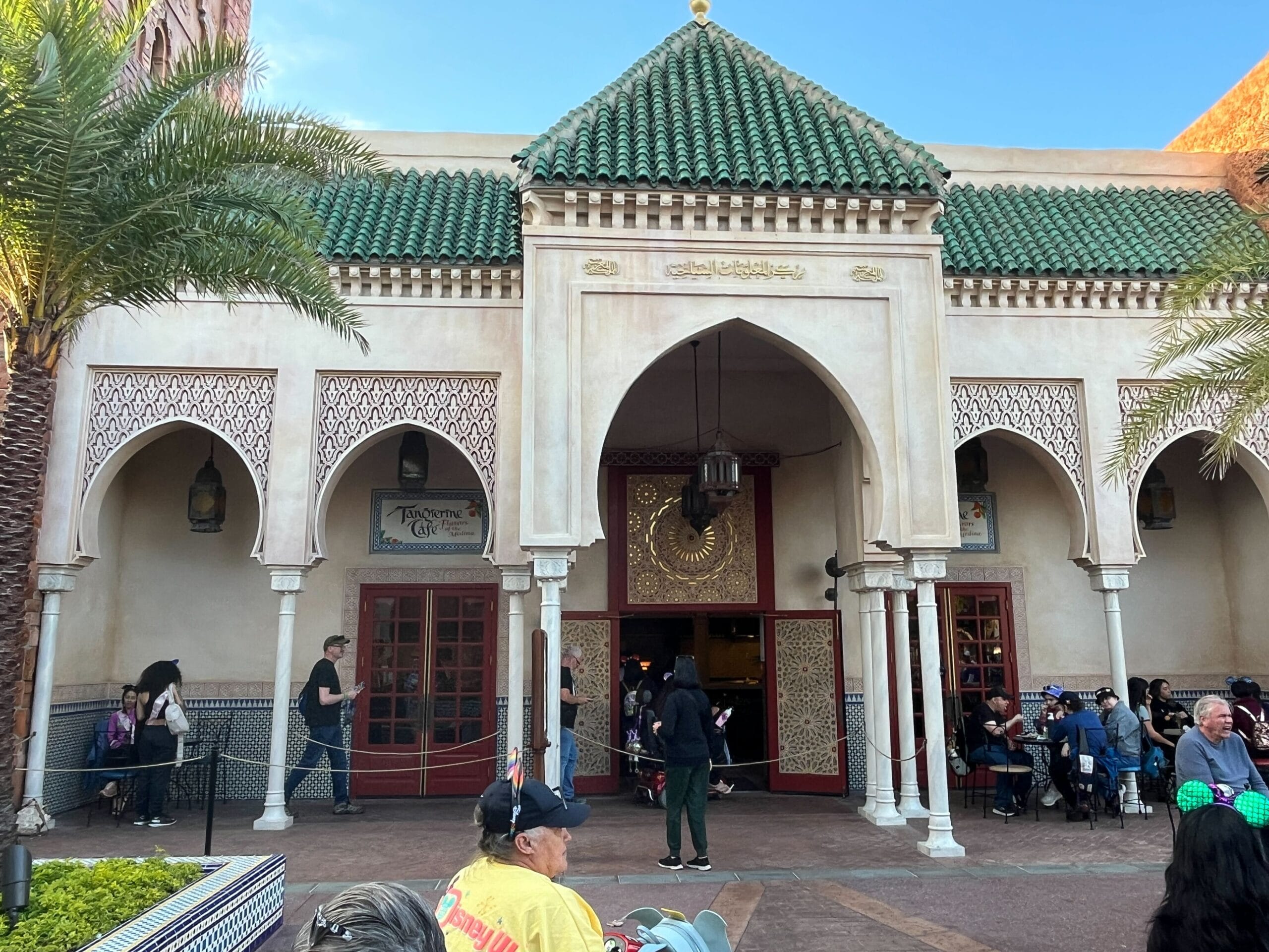 A building with ornate arches and a green-tiled roof, featuring a central entrance where people gather for the Festival of the Arts under a clear blue sky.