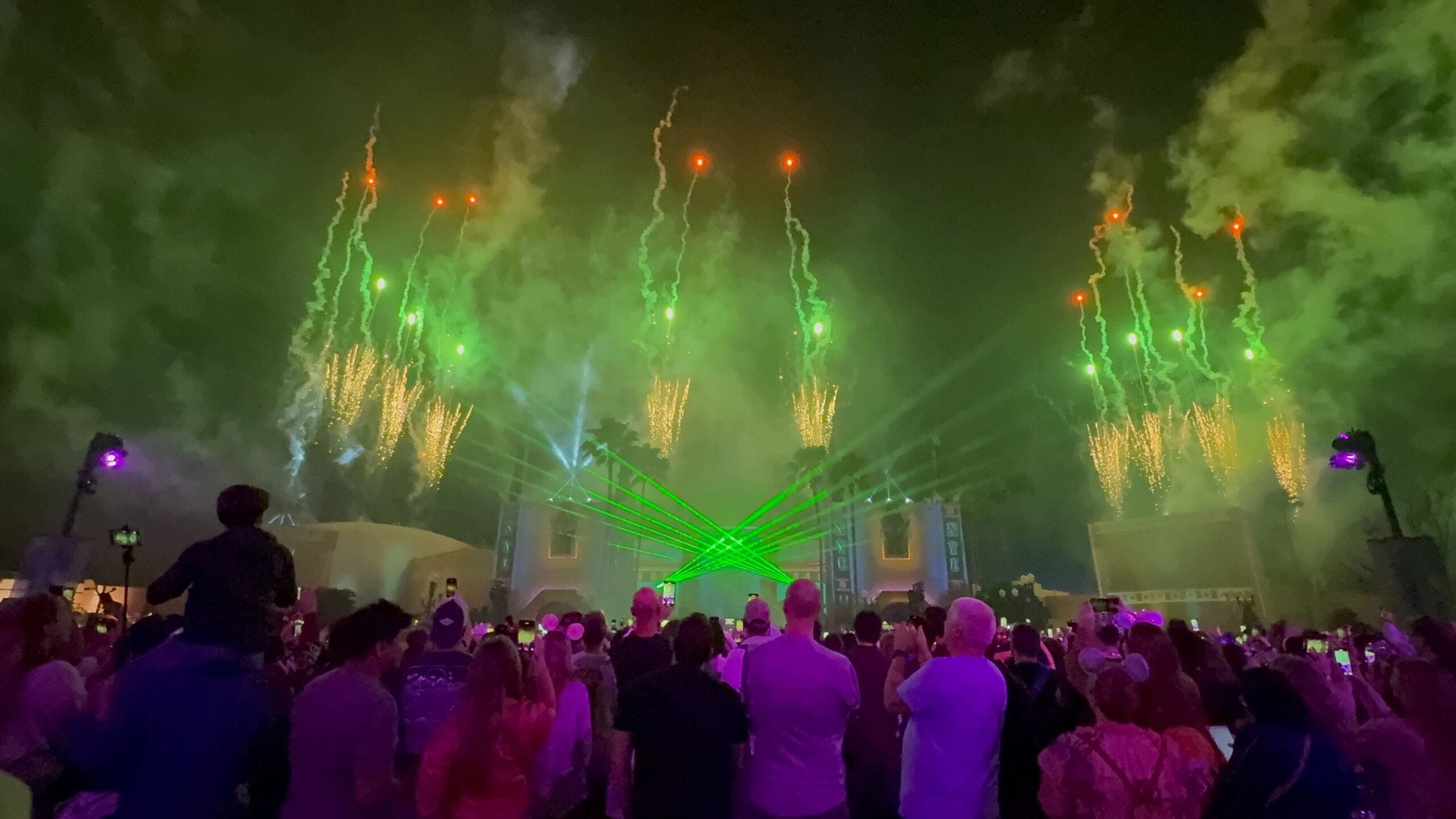 People gathered to watch a dazzling nighttime outdoor show, with green lasers painting the sky alongside breathtaking fireworks, creating an electric New Year's Eve atmosphere.