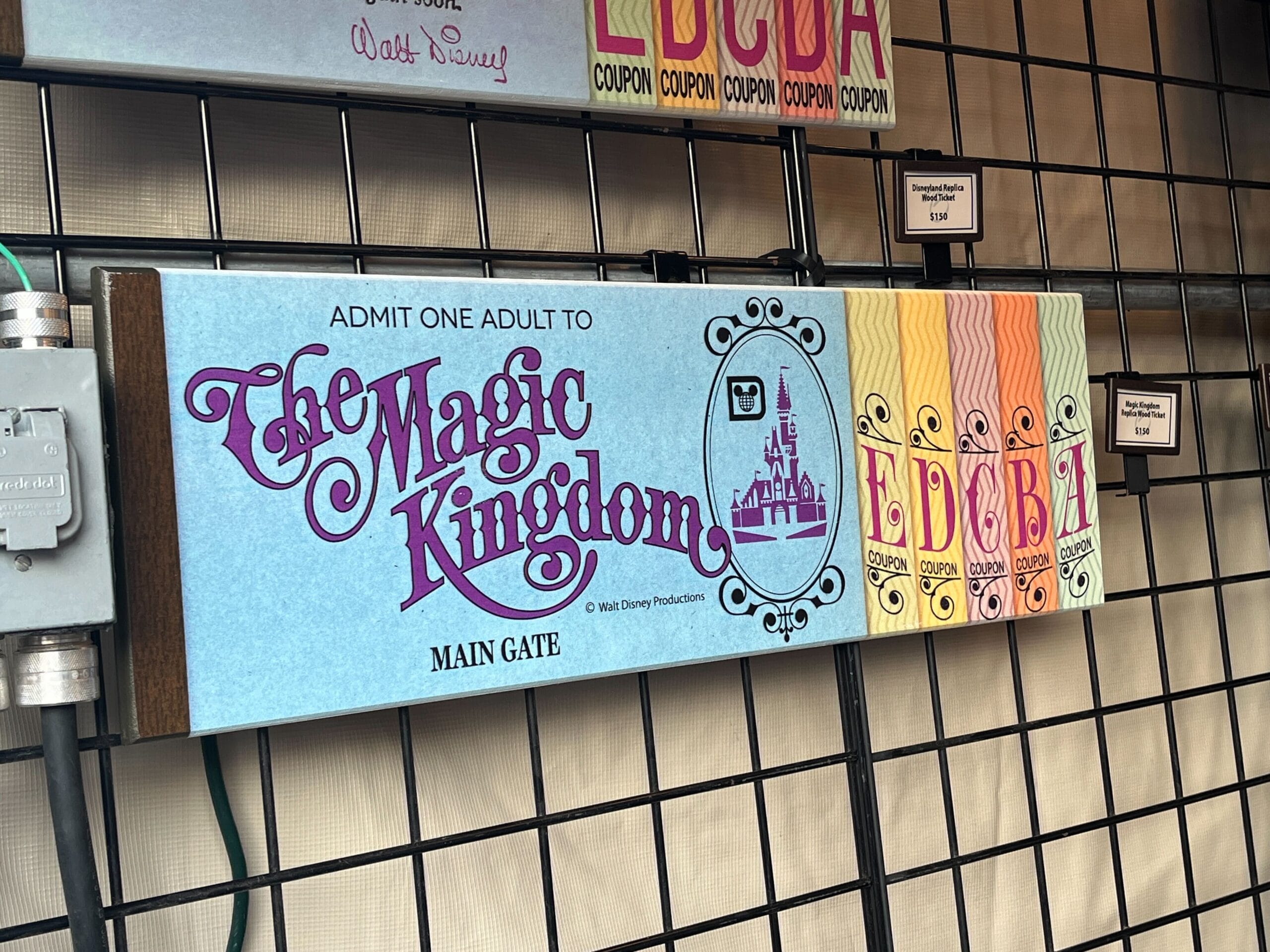 A vibrant display of vintage Disney ticket booklets on a wire grid showcases "The Magic Kingdom" on a blue cover, surrounded by colorful companions. Imagine this nostalgic collection as part of the EPCOT Festival of the Arts, perhaps curated by Dave Avanzano for a 2025 exhibition.