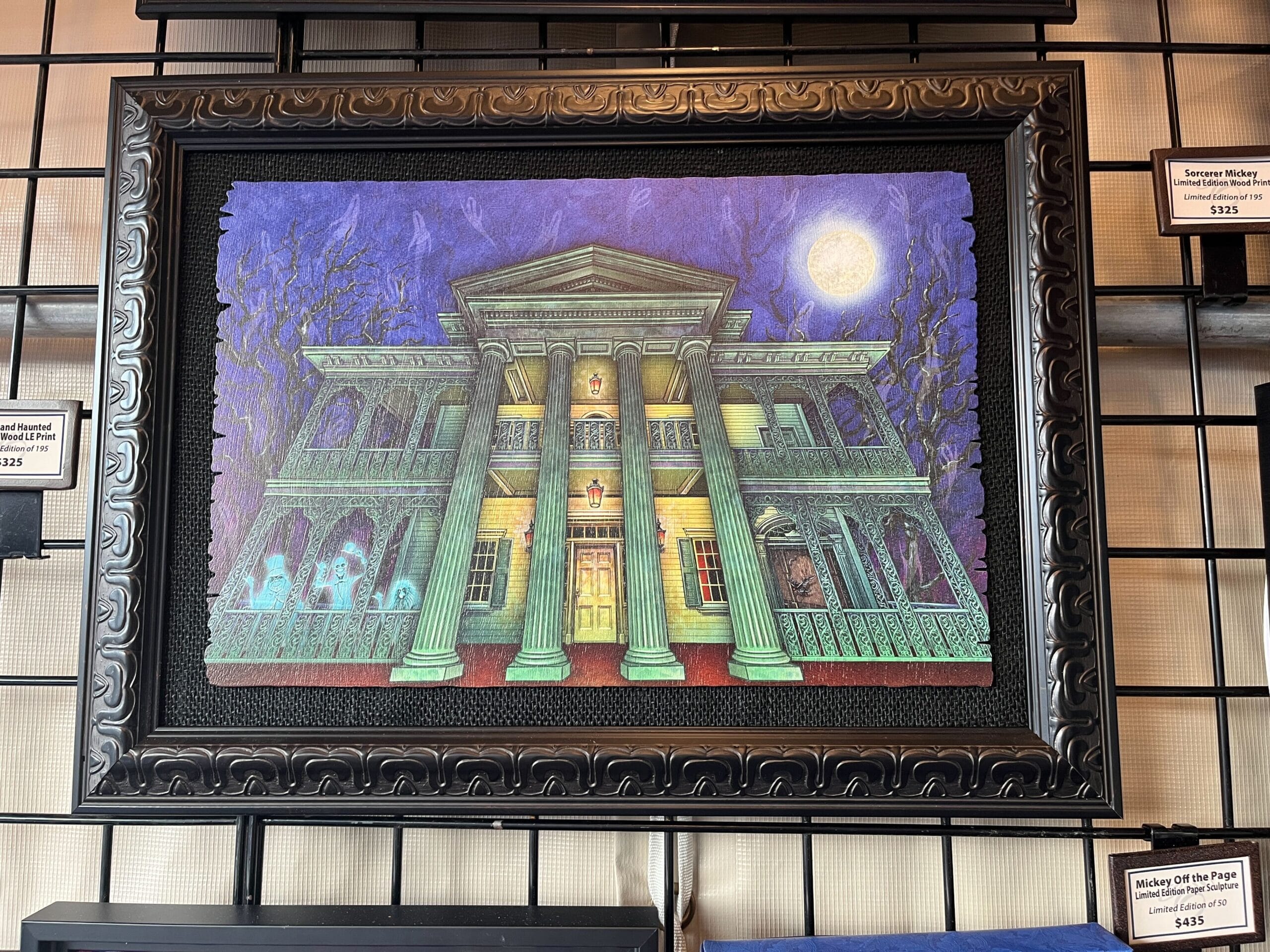 Framed painting of a haunted mansion at night, crafted by Dave Avazano for the 2025 EPCOT Festival of the Arts, with glowing windows, ghostly figures, and a full moon in the background.