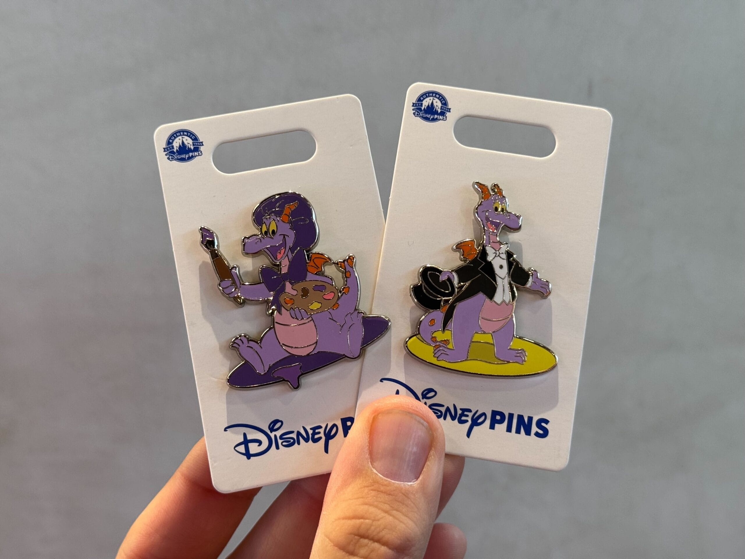 Two Disney pins featuring a purple dragon character. One shows the dragon in a whimsical pose with a cape, and the other depicts the dragon holding a staff and pumpkin.