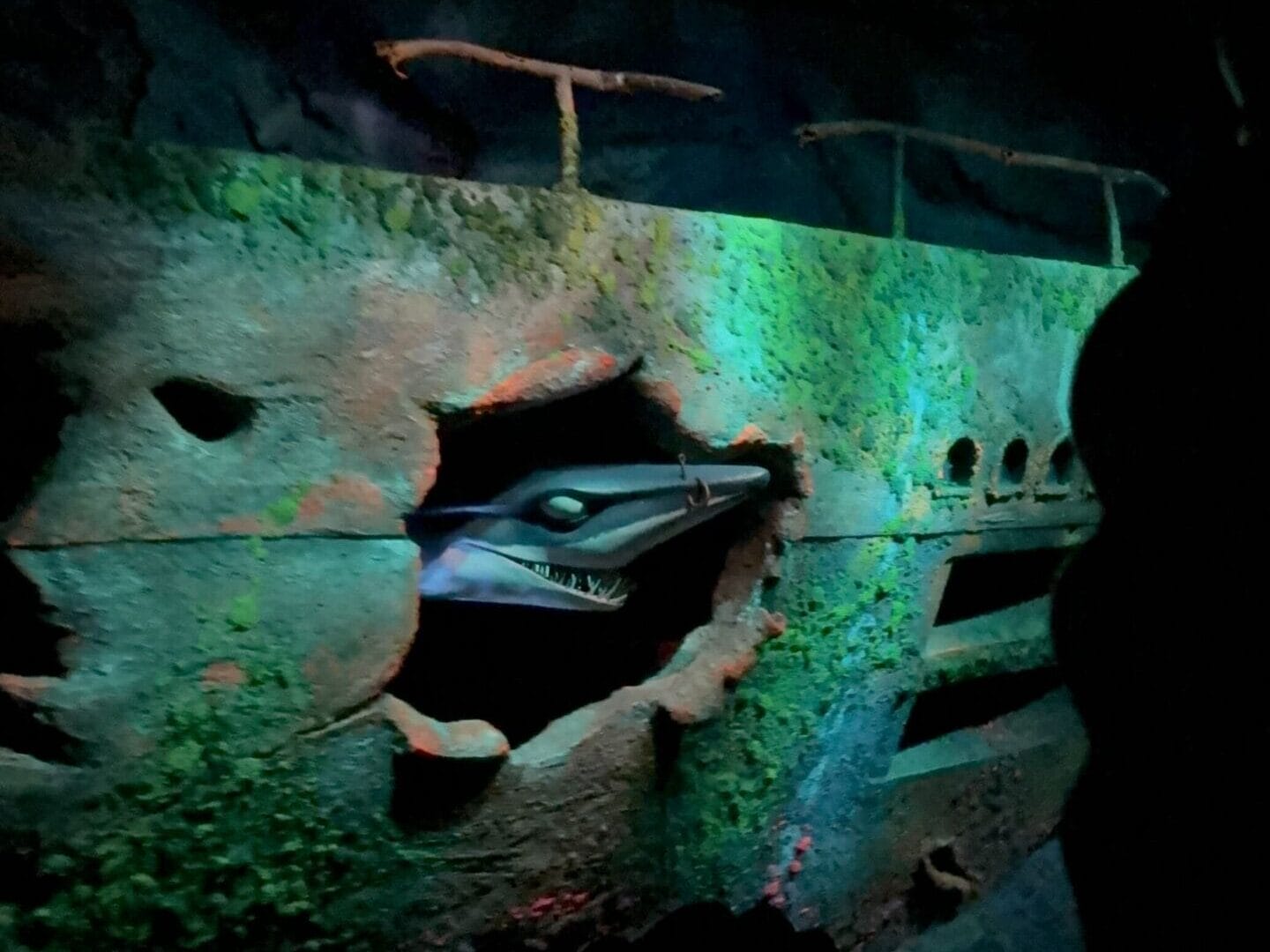 A shark with sharp teeth emerges from a sunken sub, like a scene from The Seas with Nemo & Friends at Disney World.